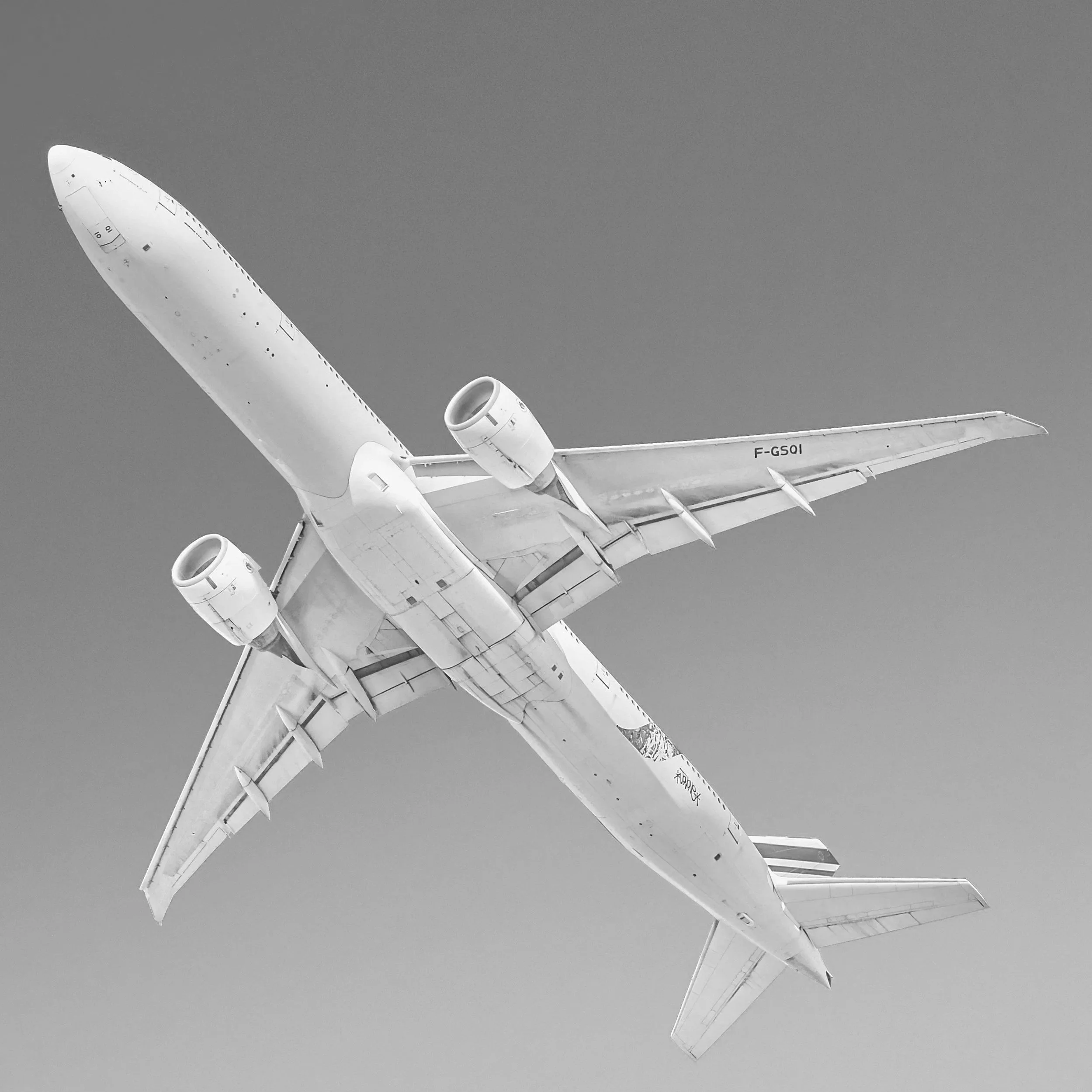 Black and white image of a commercial airplane flying in the sky, viewed from below.