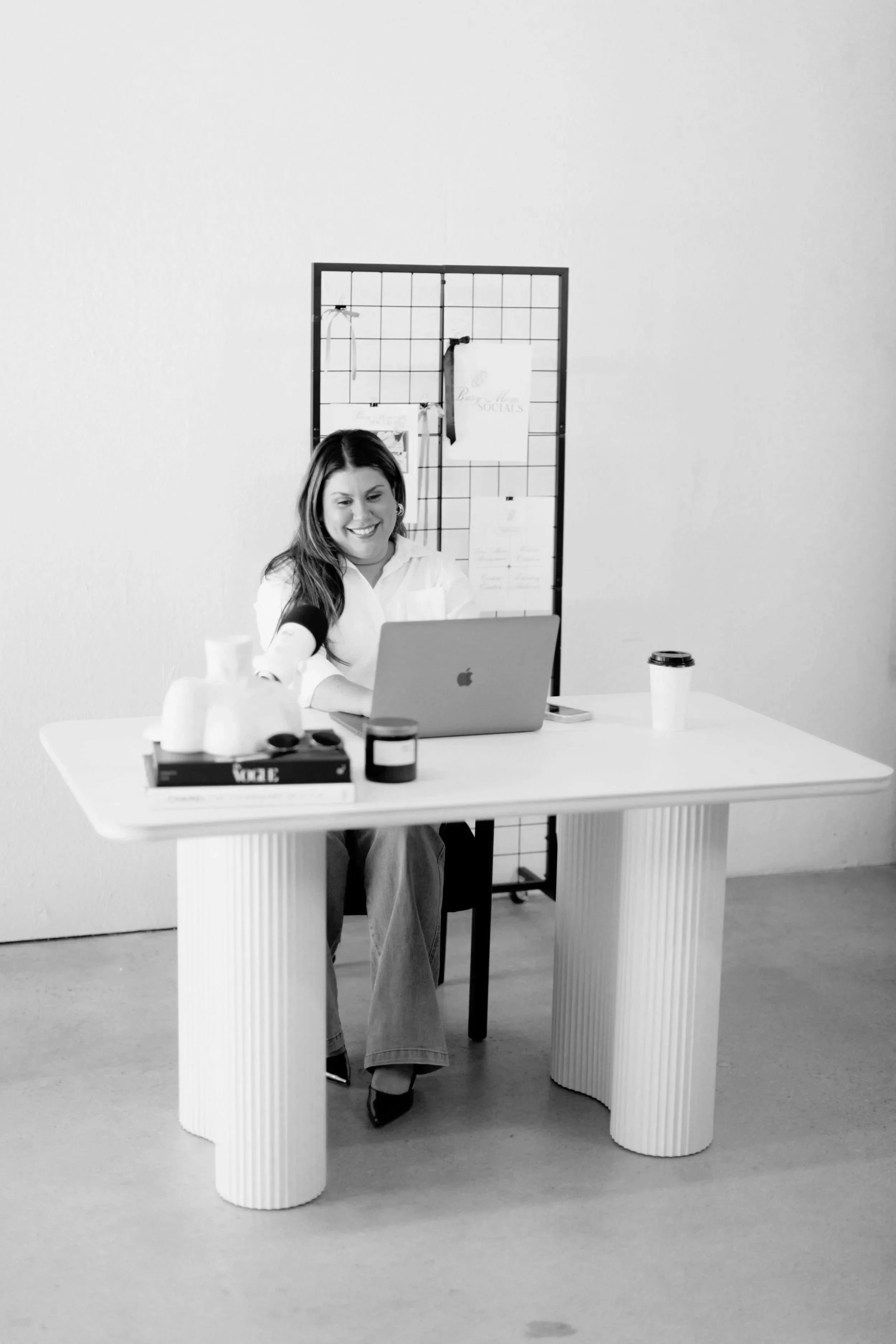 A woman sitting at a desk, working on a laptop, with a smile on her face in an office setting.