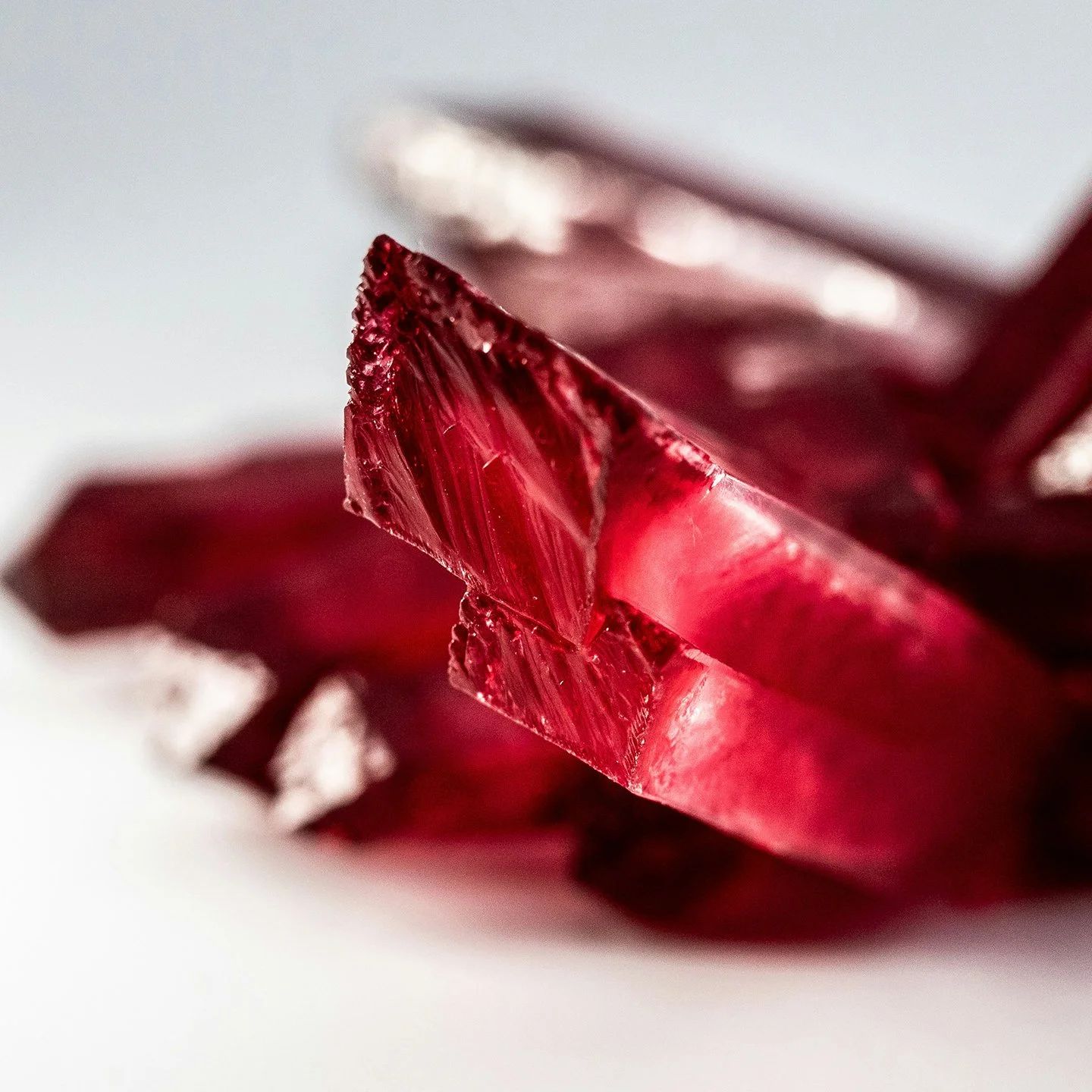 Gros plan sur un morceau de cristal rougeâtre avec une texture glacée, posé sur une surface blanche.