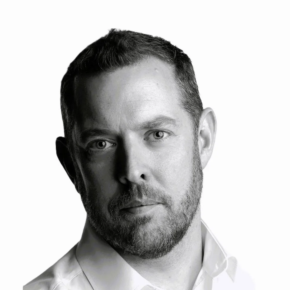 Black and white portrait of a man with short hair and a beard, wearing a collared shirt, looking directly at the camera.