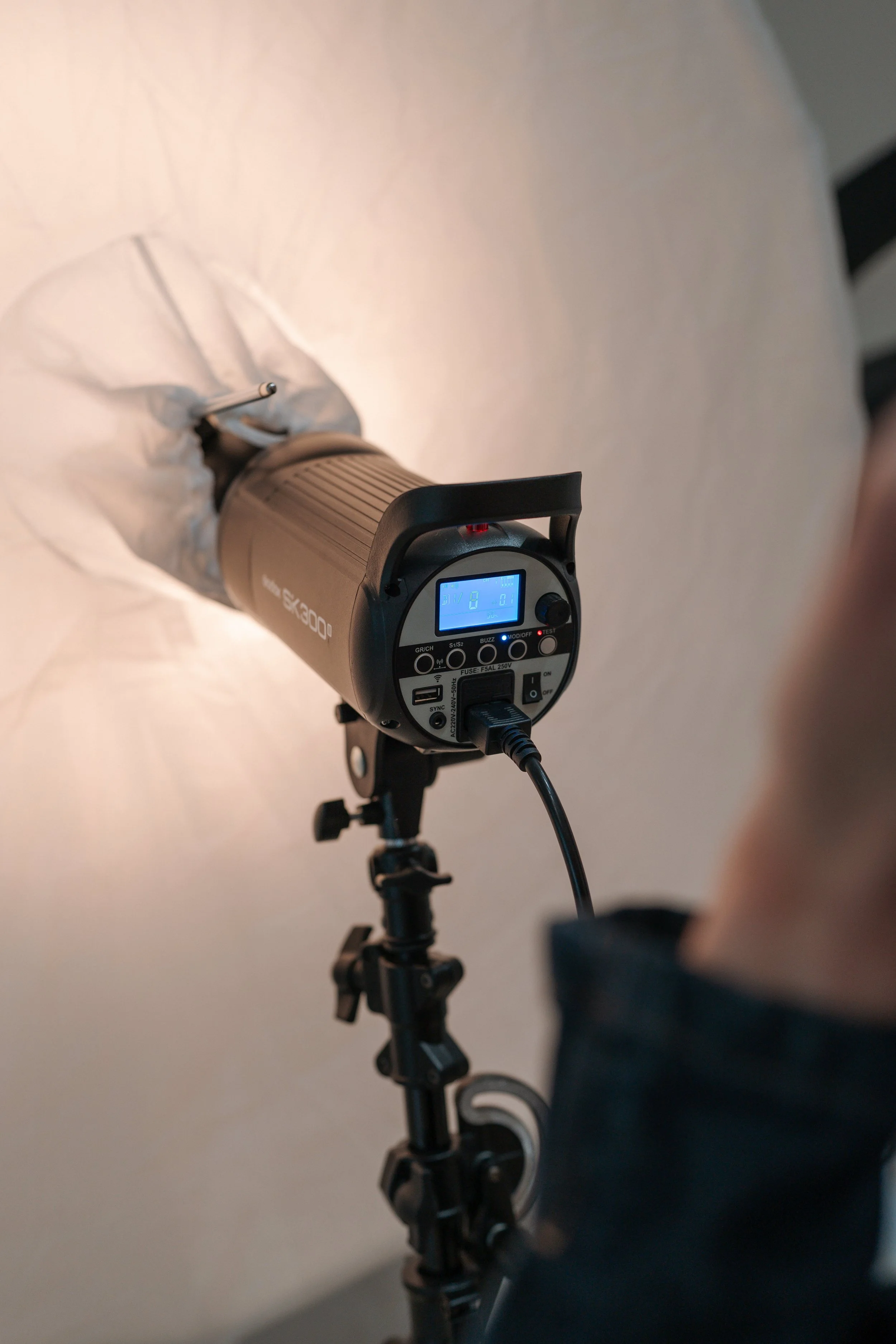 Studio strobe light with a softbox, mounted on a light stand, and a person adjusting it.