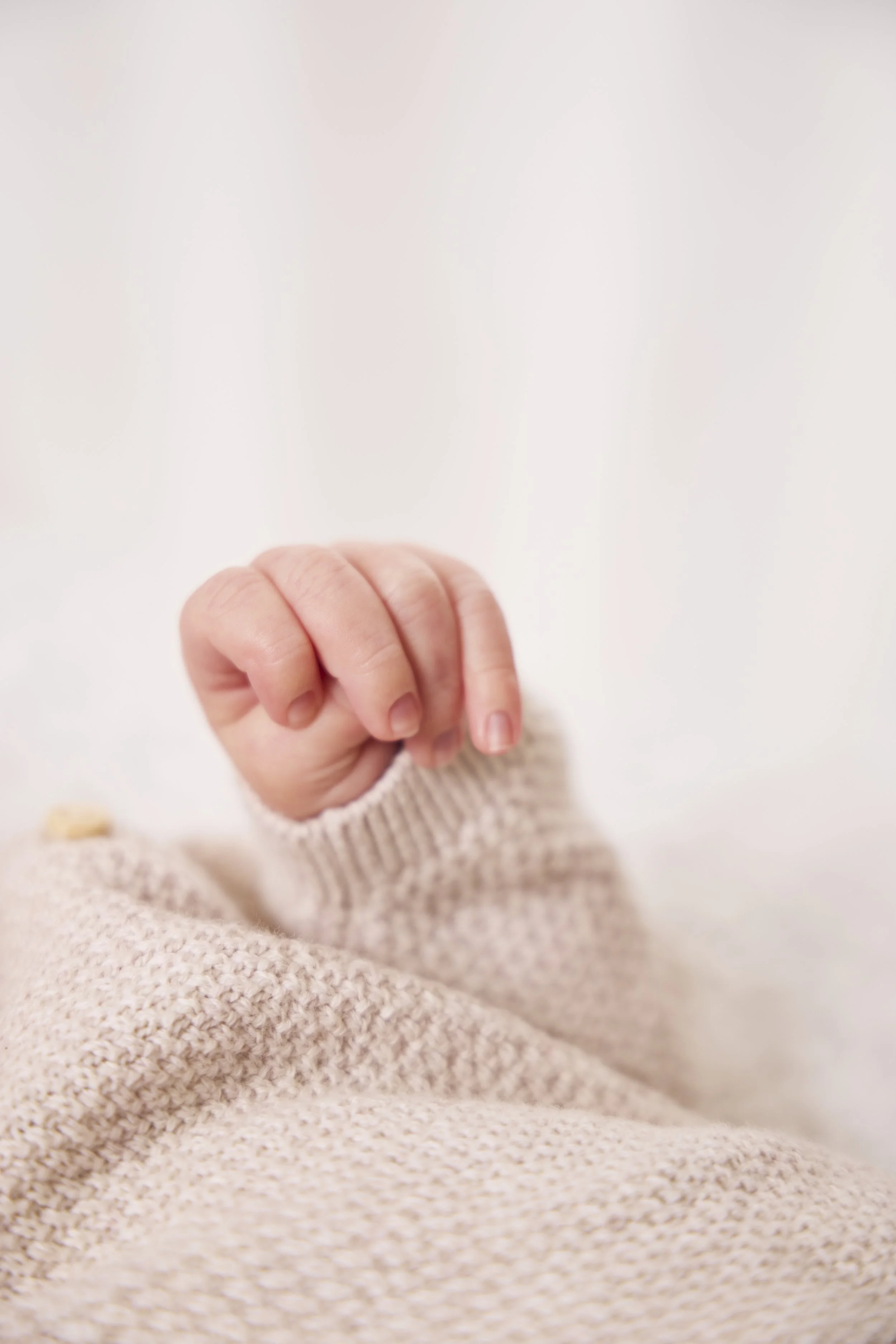 Close-up of a tiny baby hand with fingers curled, wearing a knit beige sweater.