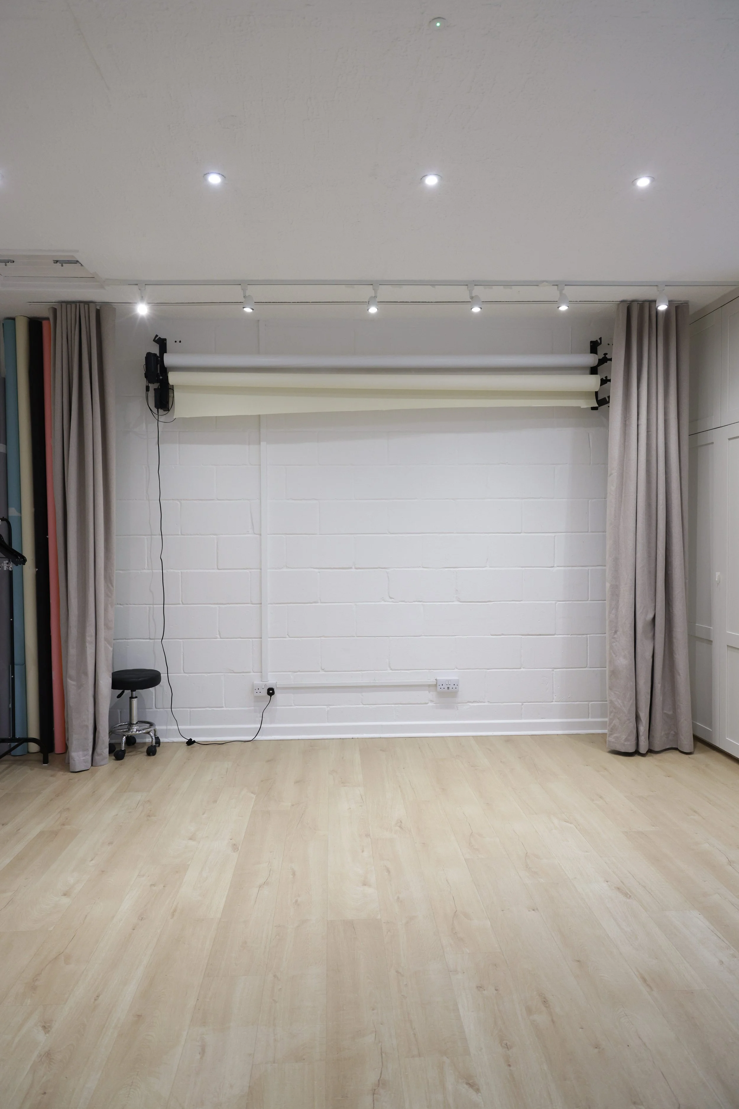 Empty photography studio with white brick wall, light wood flooring, gray curtains, and a backdrop roll.