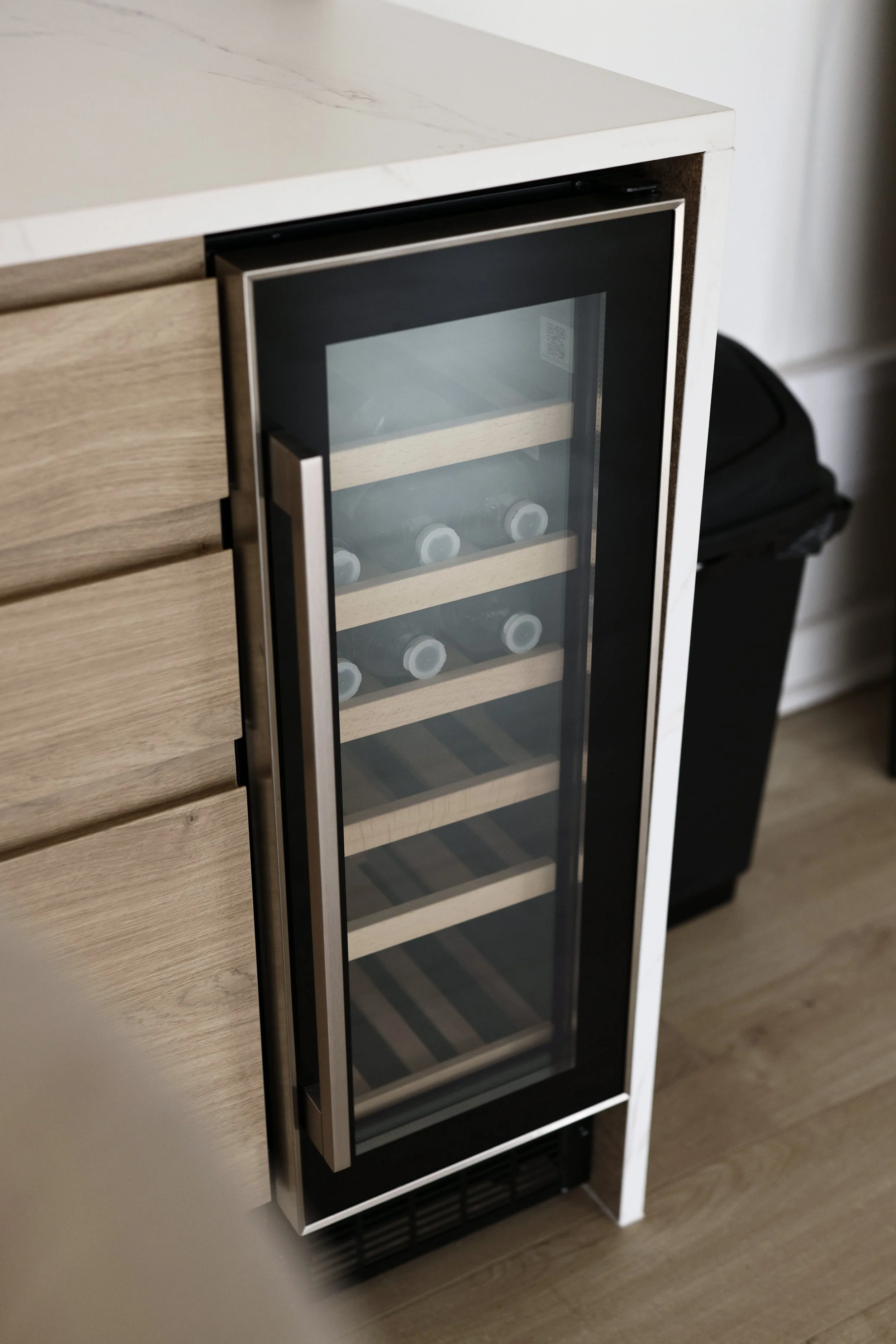A small, upright wine cooler with a glass door, containing several wine bottles stored on wooden shelves inside.
