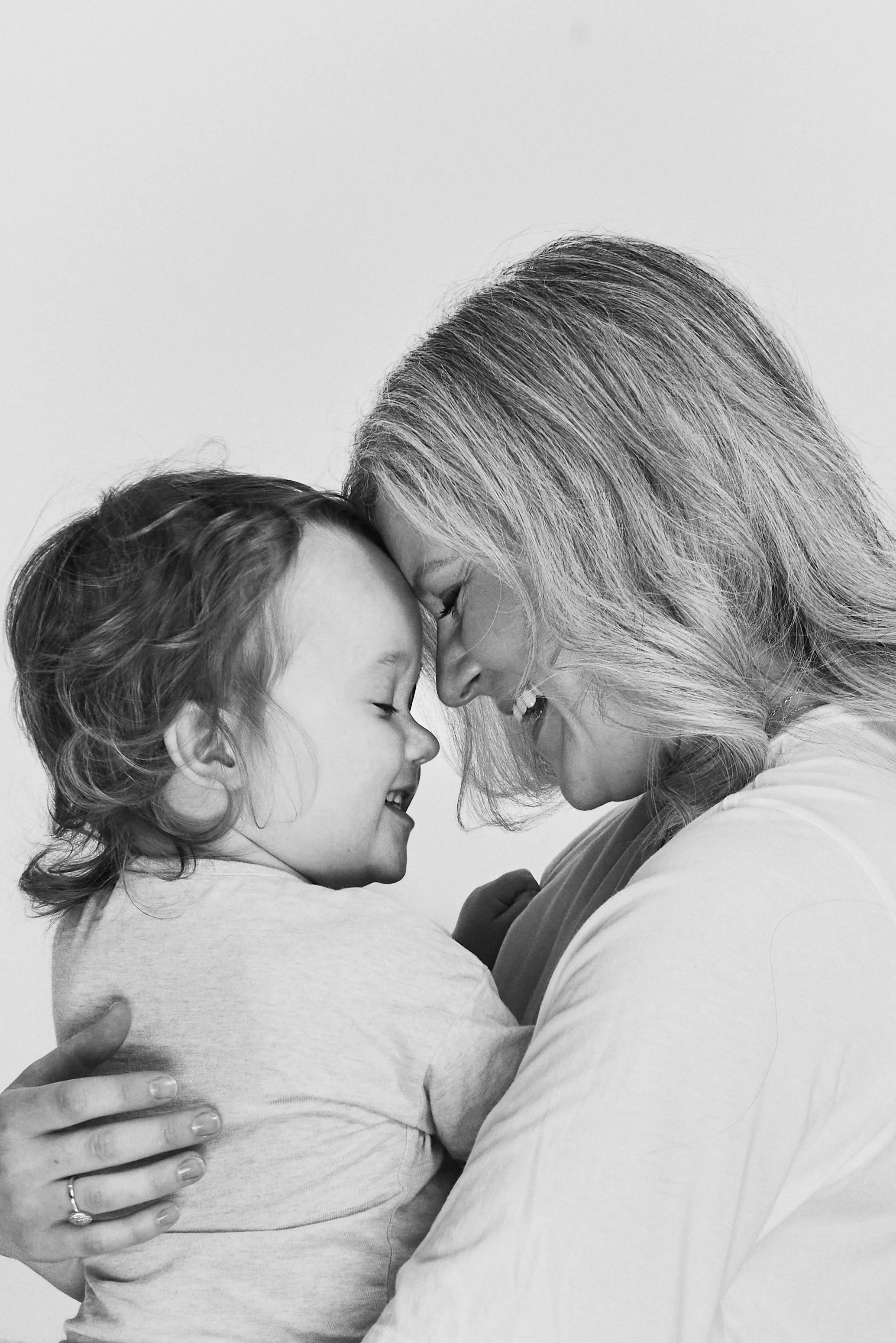 Black and white photo of a woman and young girl with foreheads touching, smiling, in a close embrace.
