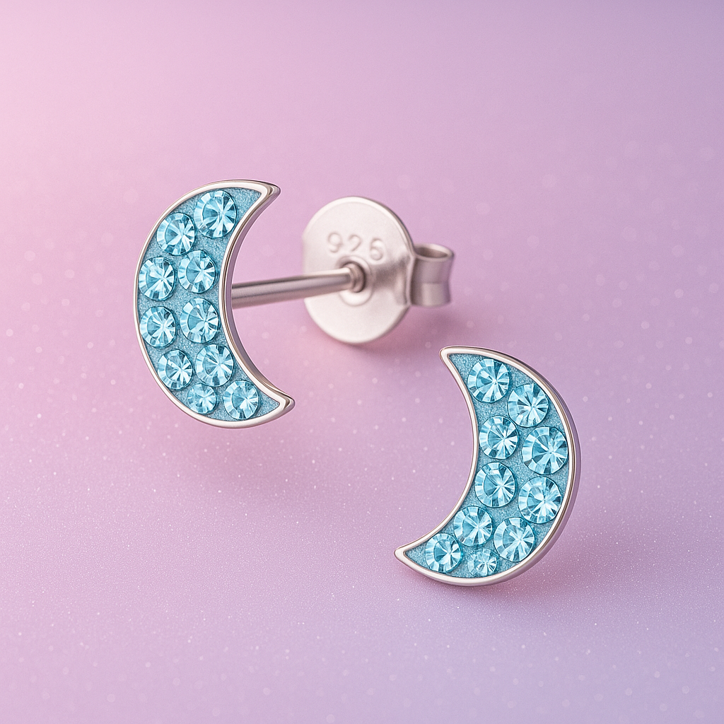 Silver moon-shaped earrings filled with light blue rhinestones on a pink glittery background.