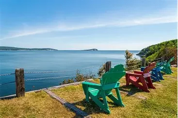 Colorful Adirondack chairs facing a large body of water and distant shoreline under a blue sky.