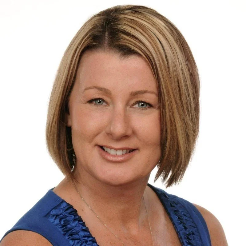A woman with shoulder-length blonde hair wearing a sleeveless blue top and smiling against a white background.