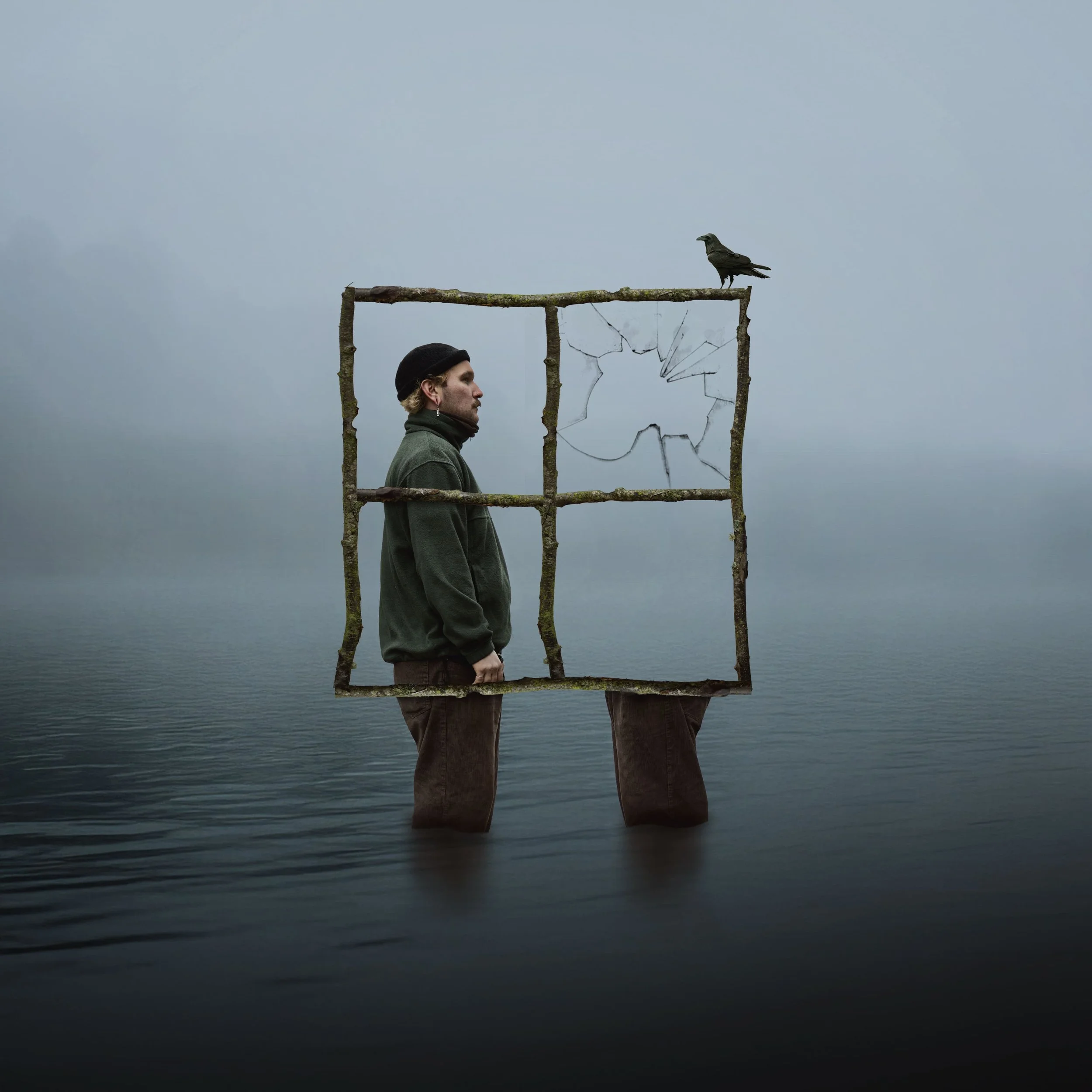 Ein Mann steht in Wasser, hinter einem eingerahmten Fensterrahmen mit zerbrochener Scheibe, auf dem ein Rabe sitzt.