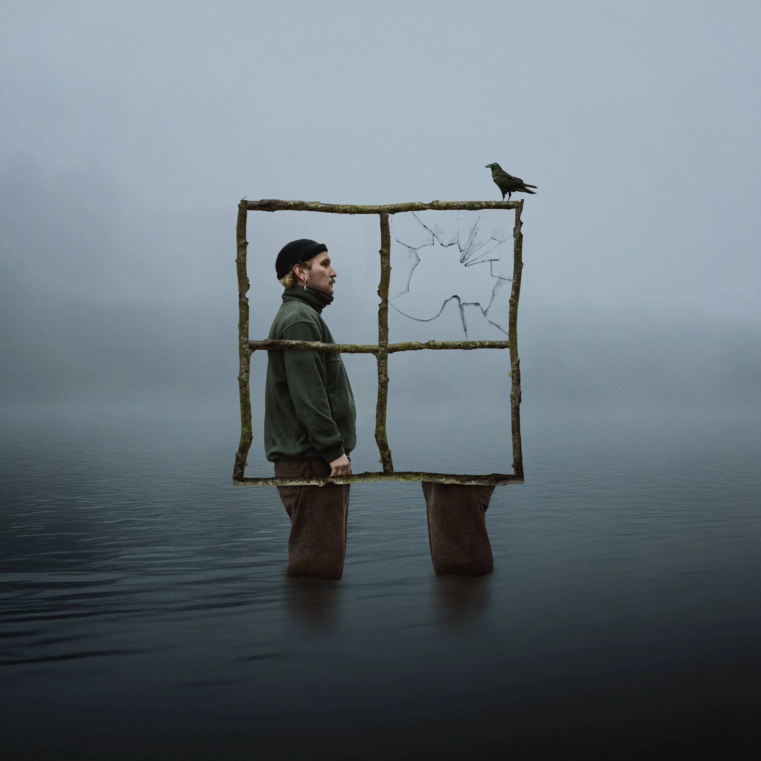 Ein Mann steht in Wasser, mit einem Rahmen aus Ästen vor ihm, der ein zerbrochenes Fenster darstellt. Auf einem Ast im Rahmen sitzt eine Krähe.