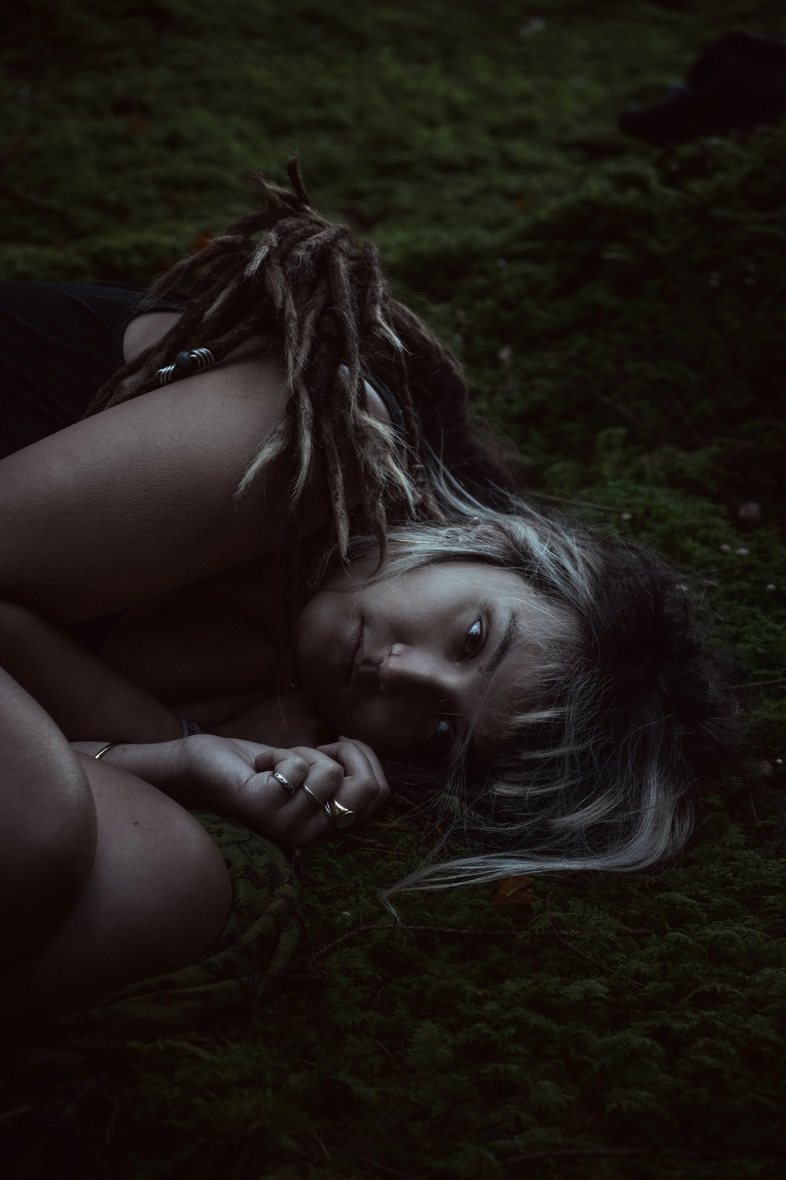 Frau mit dreadlocks liegt auf dem Waldboden und schaut in die Kamera, umgeben von grünem Moos.