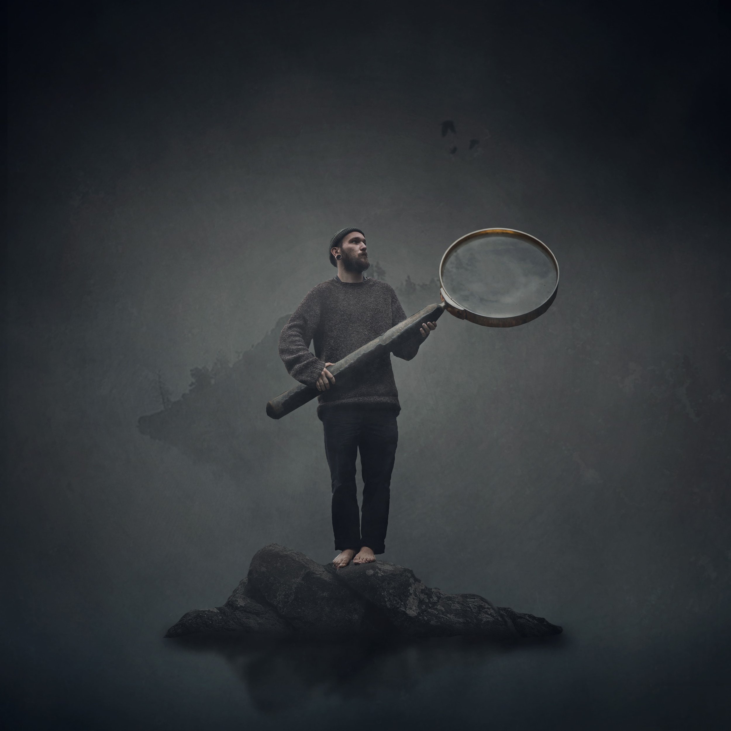 Mann steht auf einem Felsen und hält eine große Lupe, Blick in die Ferne, wolkiger Himmel im Hintergrund