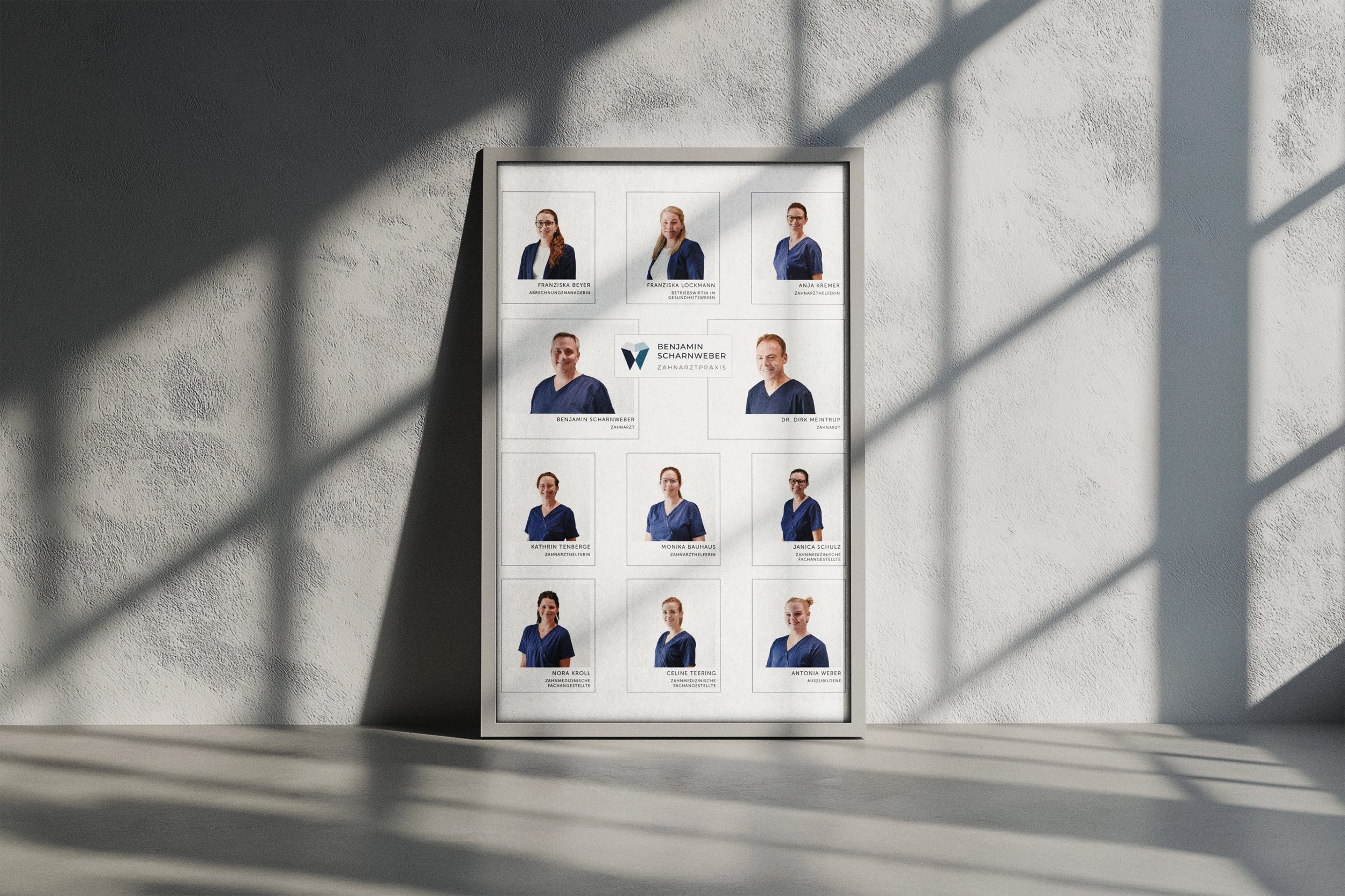 Framed display of a team photo or staff directory, featuring twelve individuals dressed in blue scrubs, with names and titles below each photo, set against a white textured wall with shadows cast from window panes.
