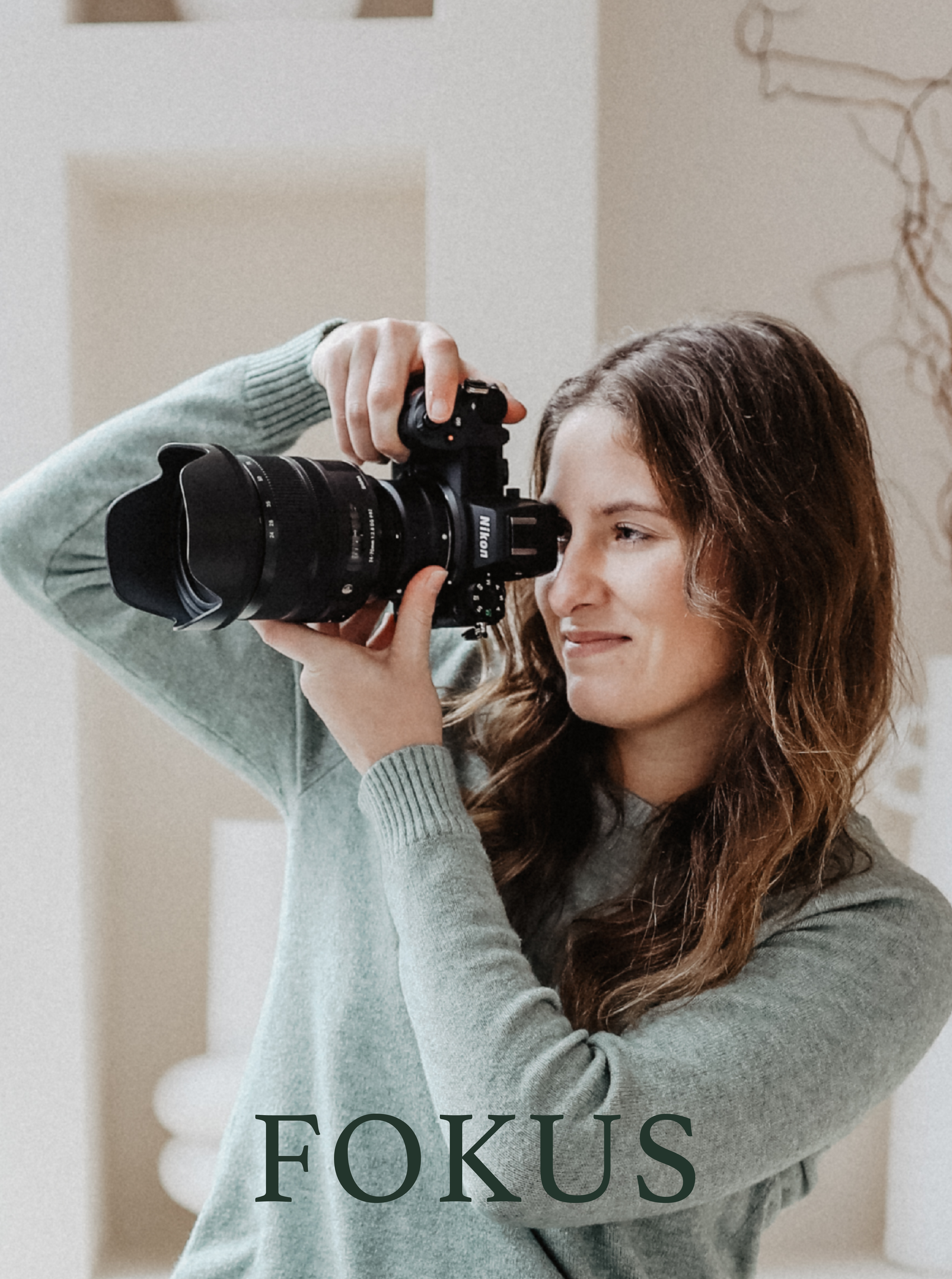 Eine Frederike mit welligem braunem Haar hält eine Nikon-Kamera vor ihr Auge und fokussiert eine Aufnahme in einem Innenraum.