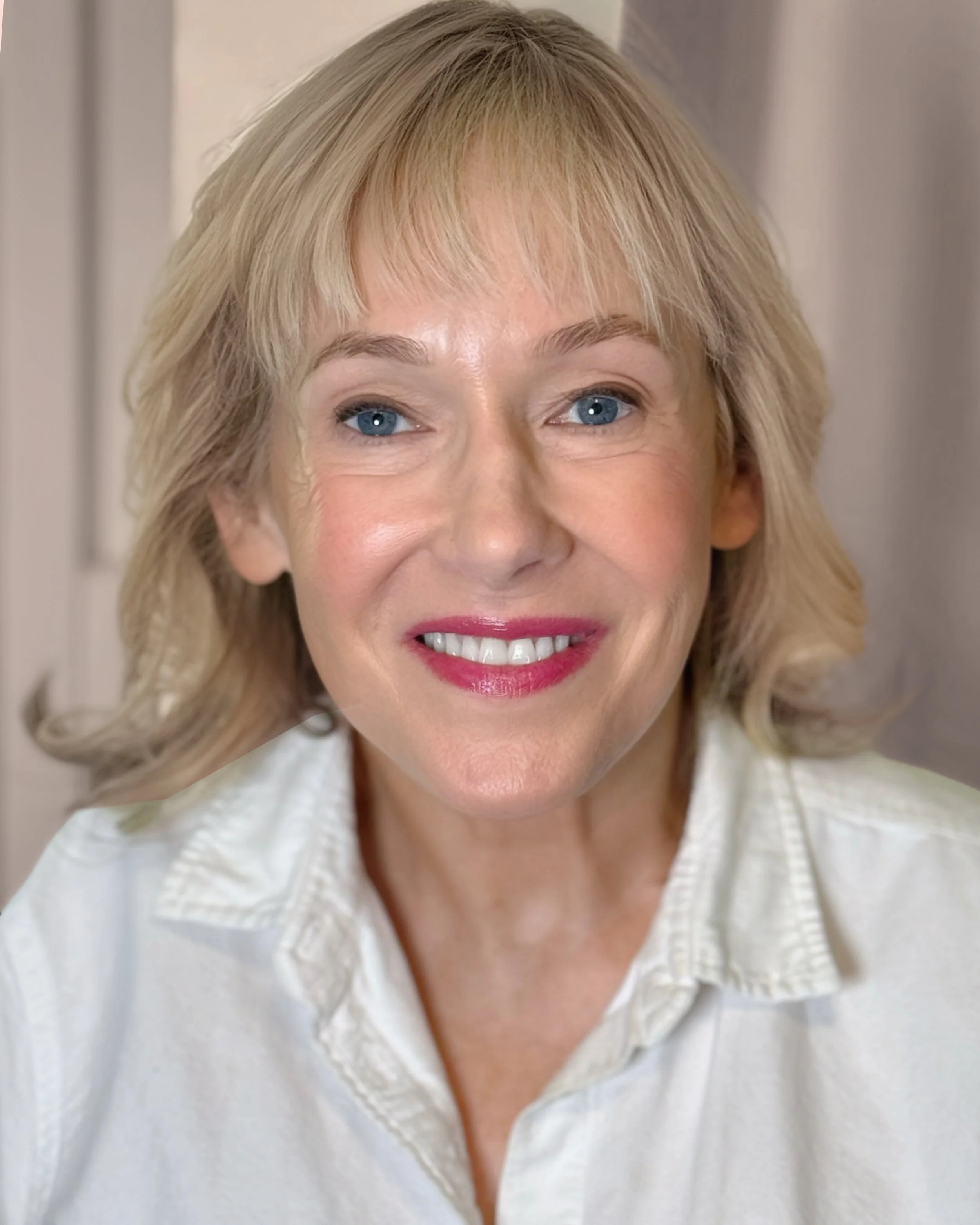 Close-up of a smiling woman with blonde hair, blue eyes, wearing a white shirt.