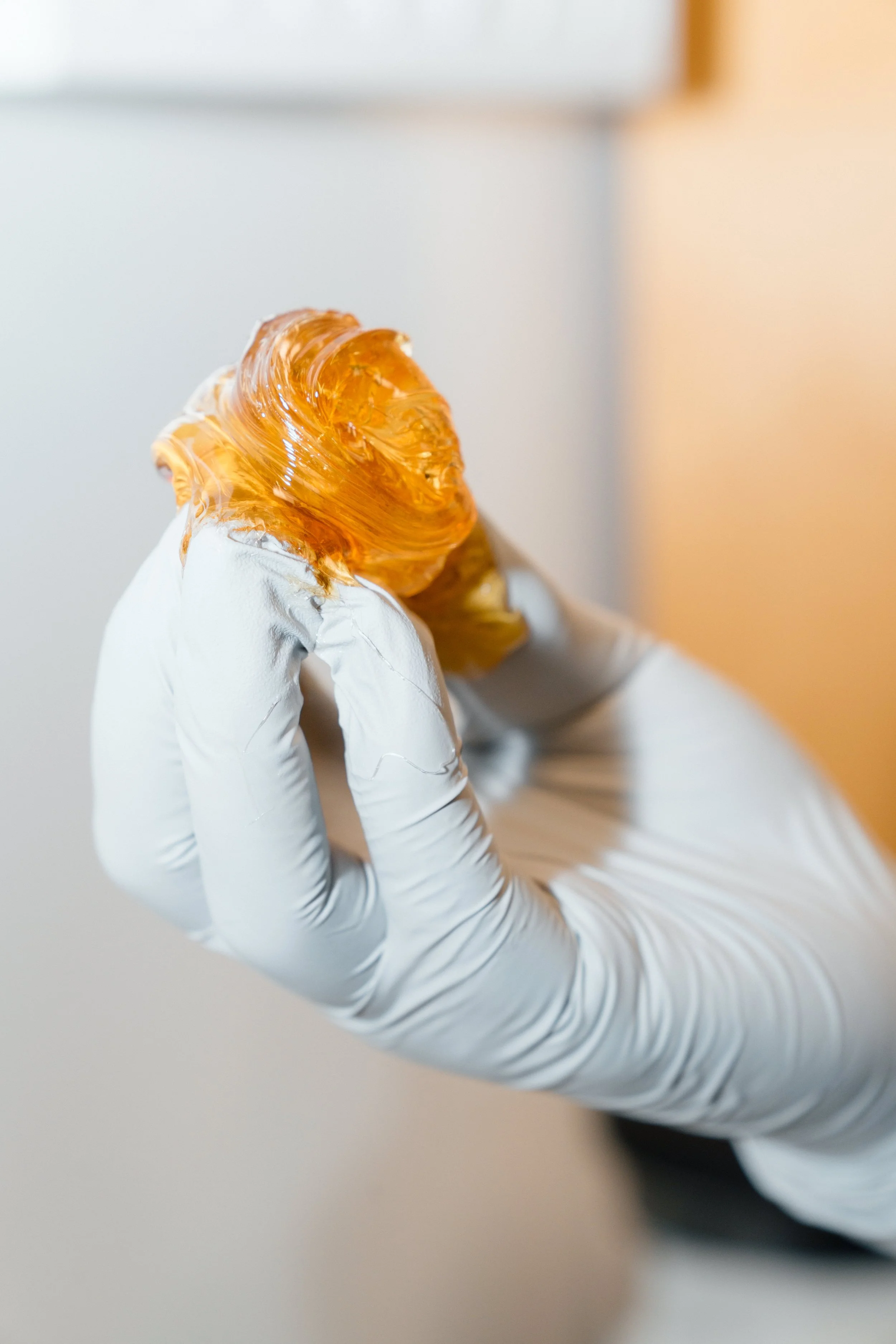 Close-up of a gloved hand holding an amber-colored glass sculpture.