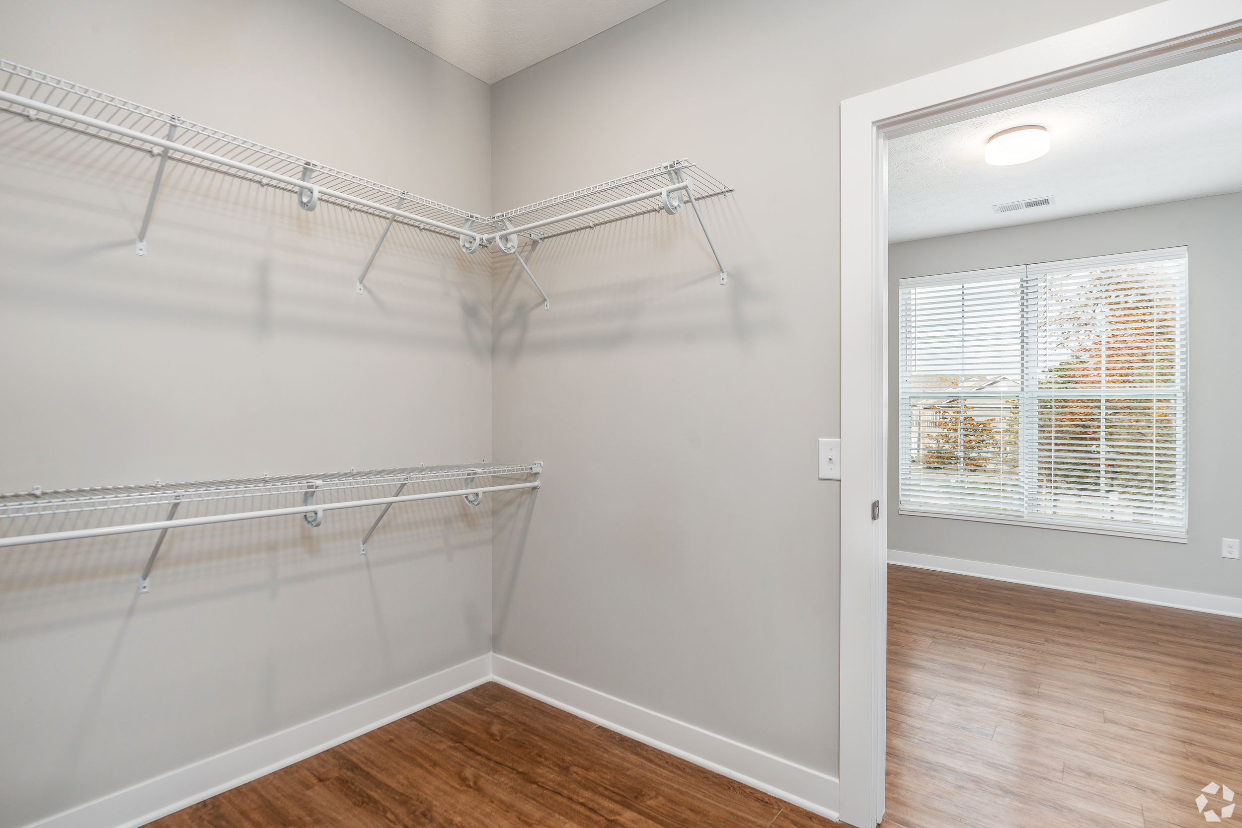 Empty walk-in closet with white wire shelves and a window with blinds.