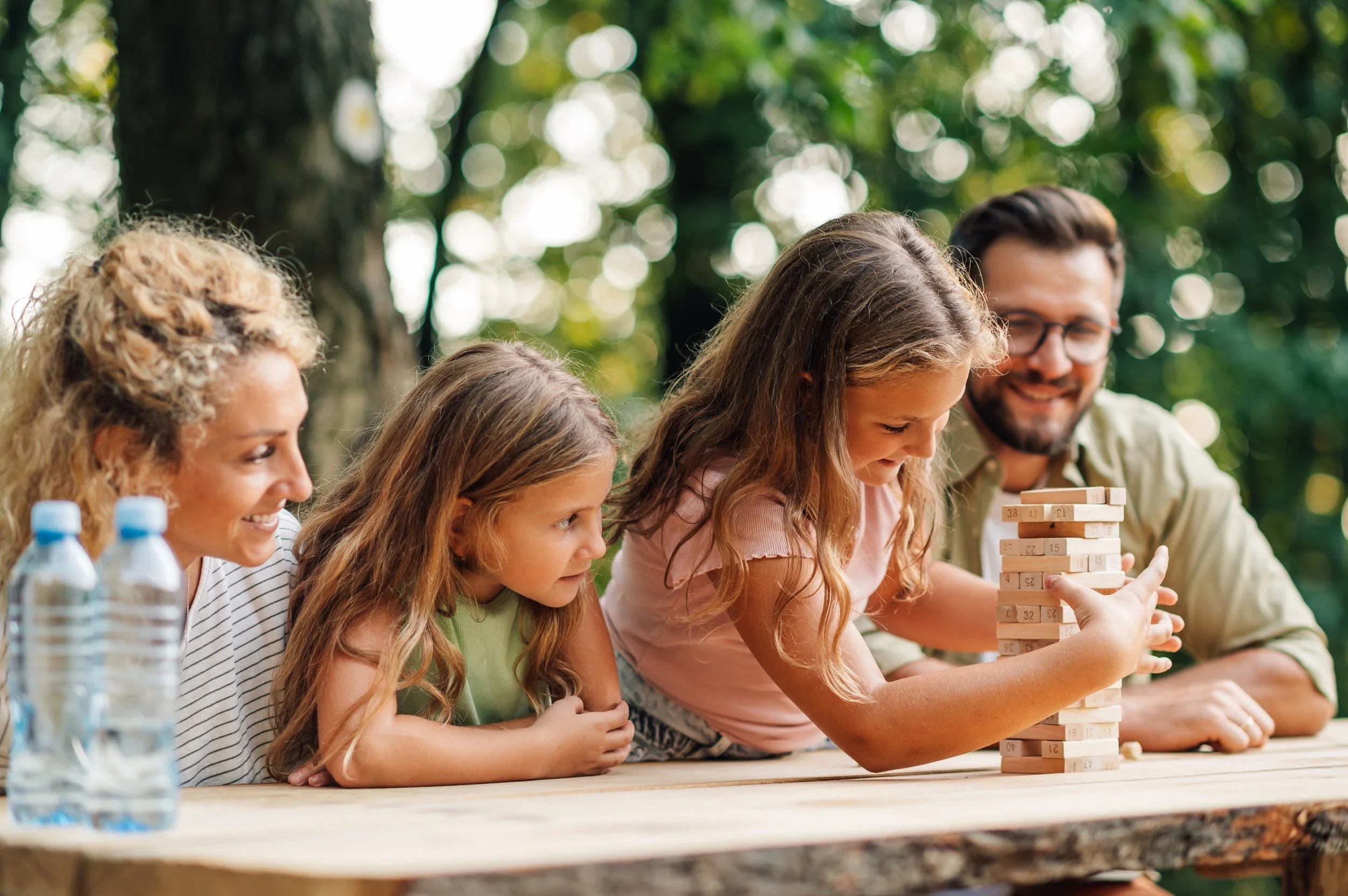Family and children playing Jenga outdoors at a park.