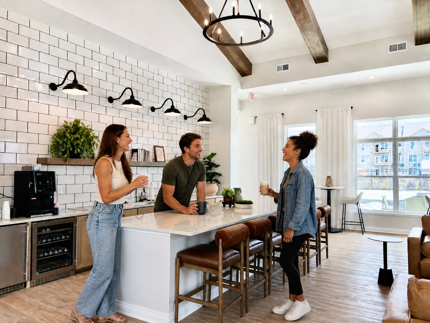 Three people chatting and smiling in a modern kitchen with white brick wall, wooden ceiling beams, large windows, and bar stools, while holding drinks