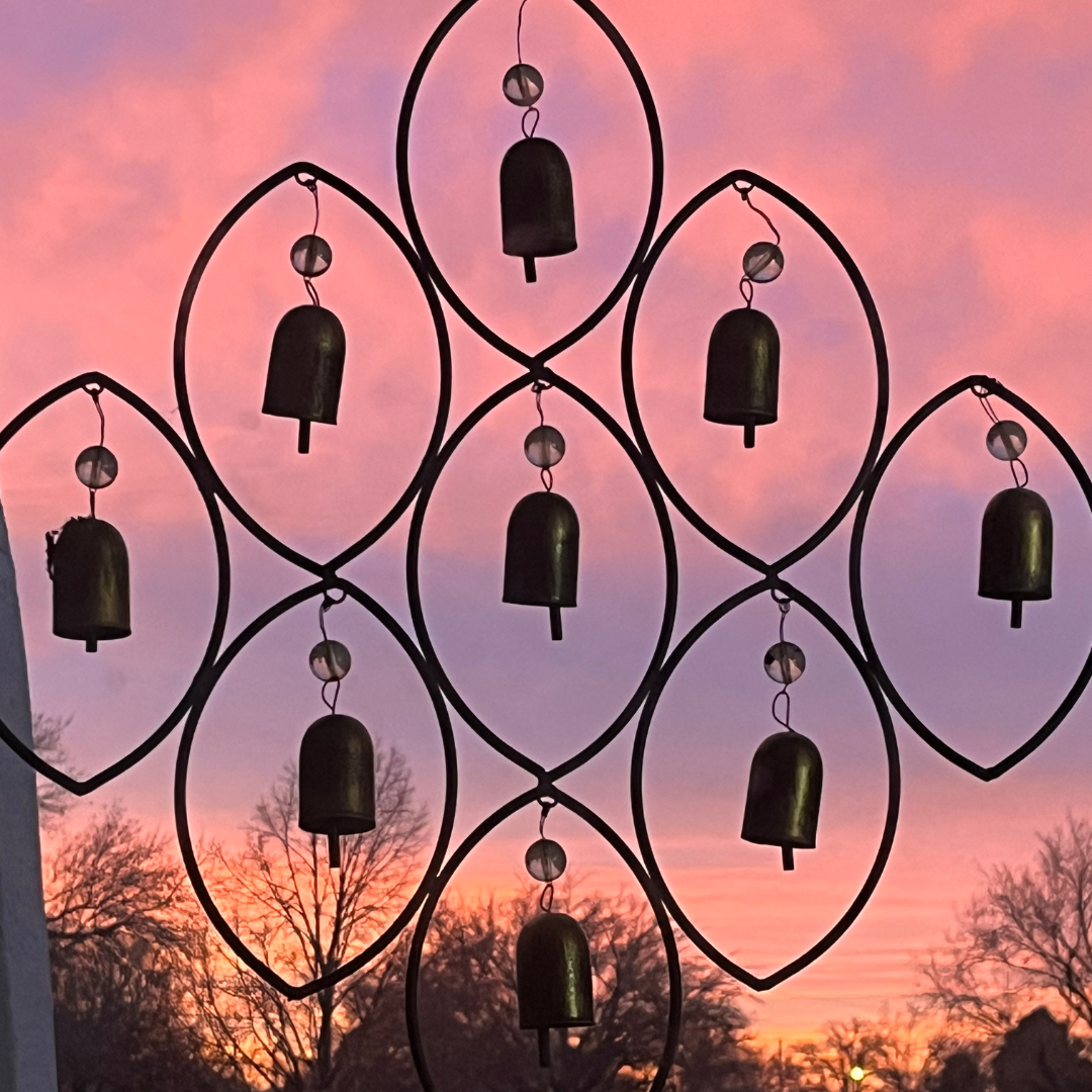 Multiple black wind chimes hanging in front of a pink and purple sunset sky, with silhouette trees in the background.