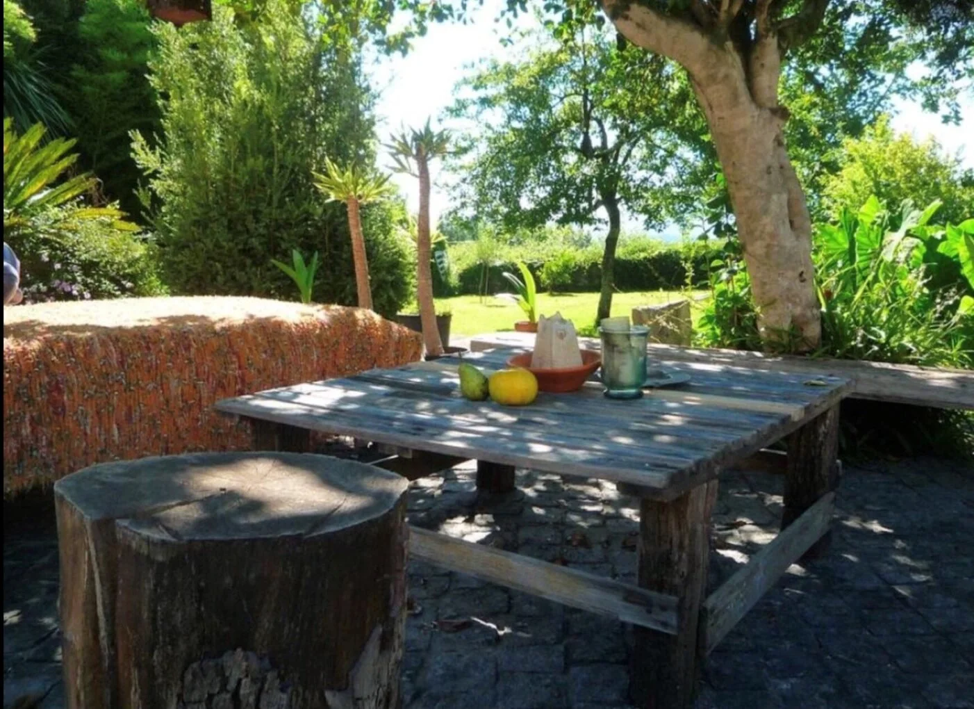 Outdoor rustic table with fruits and candles in a garden shaded by trees and lush greenery in Portugal.
