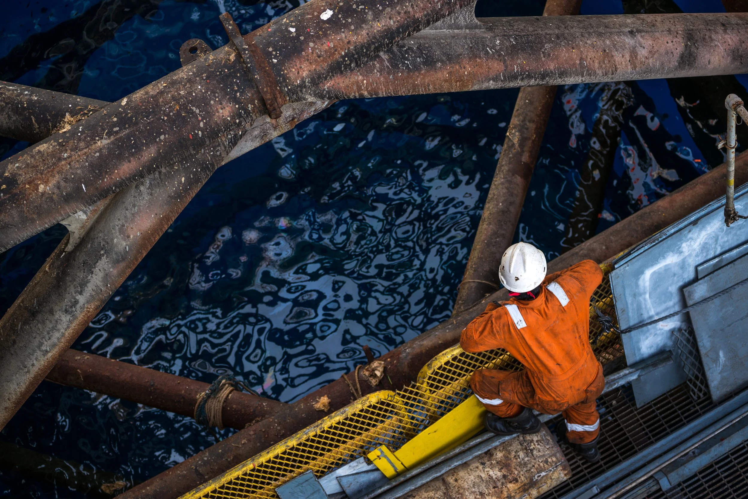 Offshore oil and gas worker in orange coveralls climbing rig platform above open water, representing EOS Permian’s rapid-response mitigation solutions for high H₂S environments.