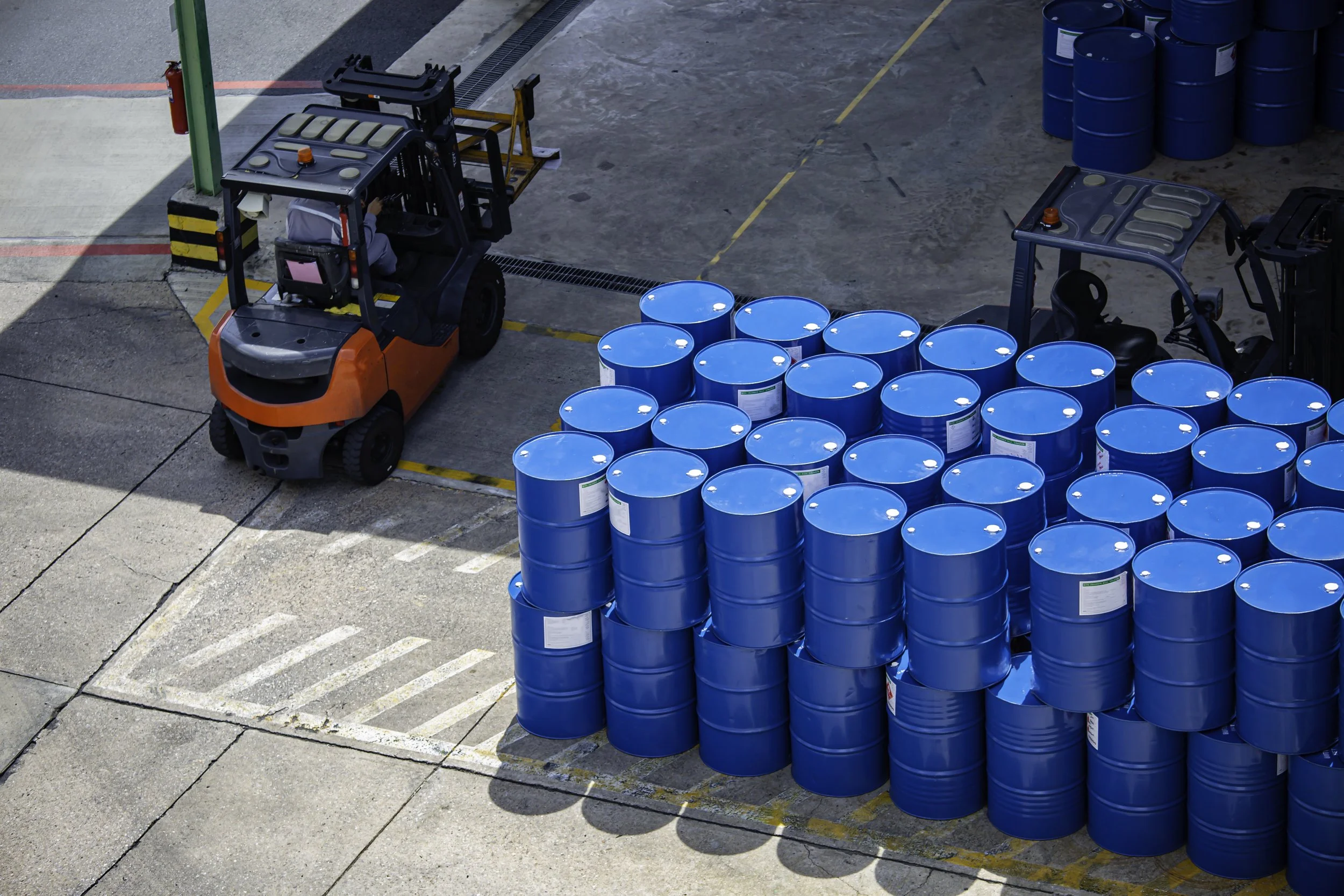 Warehouse scene with stacked blue chemical drums and forklifts in operation, representing EOS Permian’s integrated chemical platform delivery for upstream, midstream, and remediation environments.