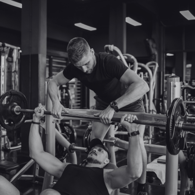 A man spotting another man lifting weights at the gym.