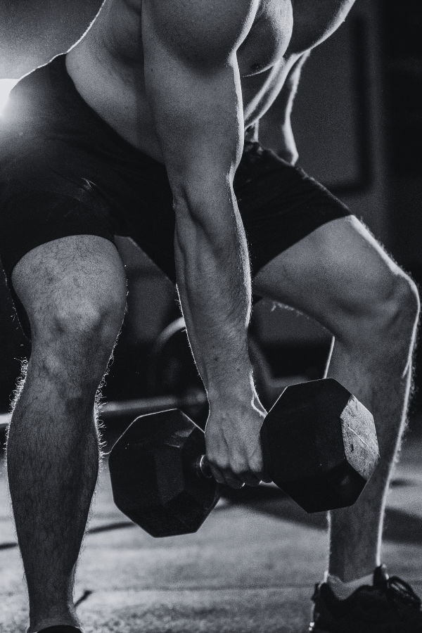 Male person in workout shorts lifting a dumbbell in a gym setting.
