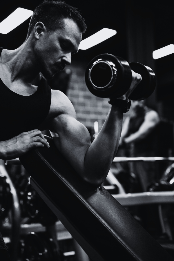 A man lifting a dumbbell in a gym, focusing on his biceps, with gym equipment in the background.