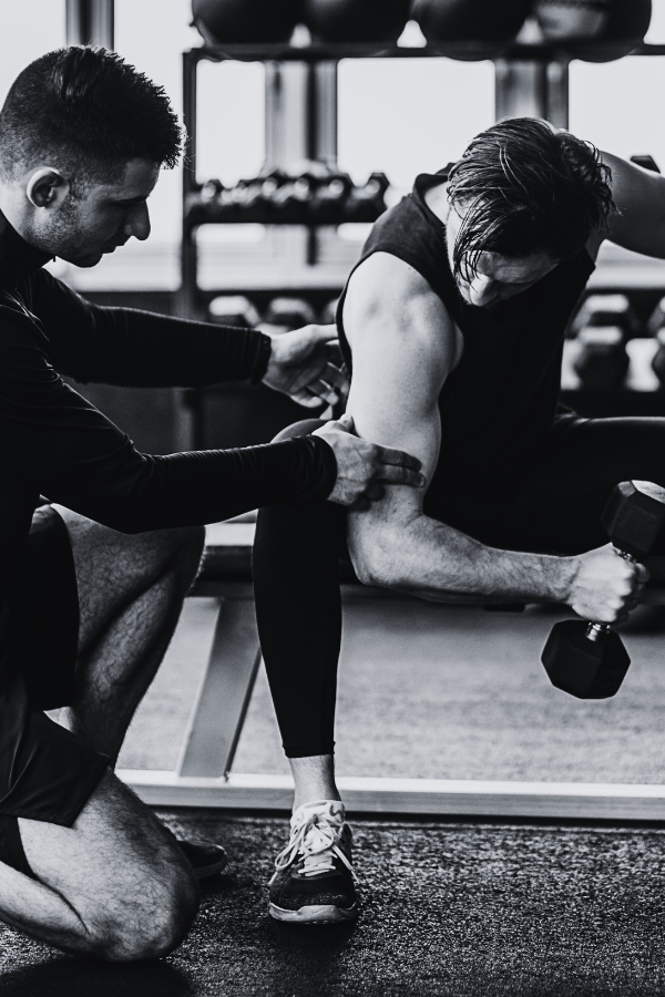 Personal trainer assisting a man with a bicep curl exercise at gym.