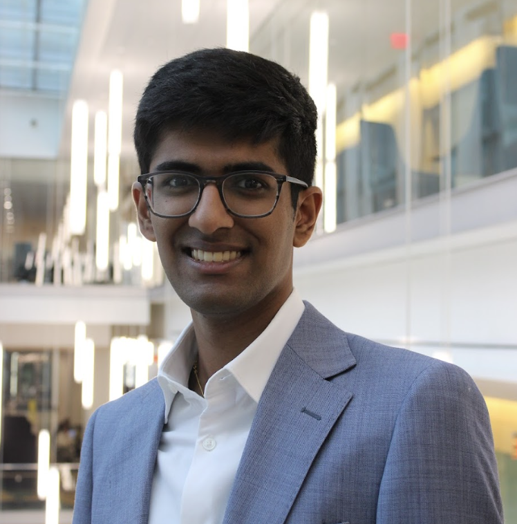 Young man in a suit and glasses smiling in a modern interior space.