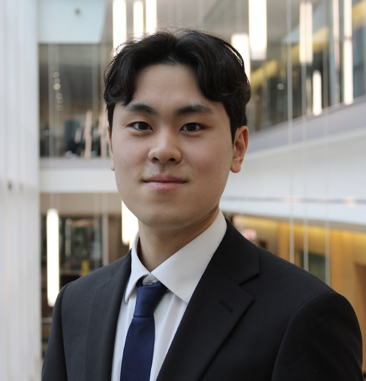 Professional young Asian man in suit and tie standing indoors with glass walls and modern architecture in the background.