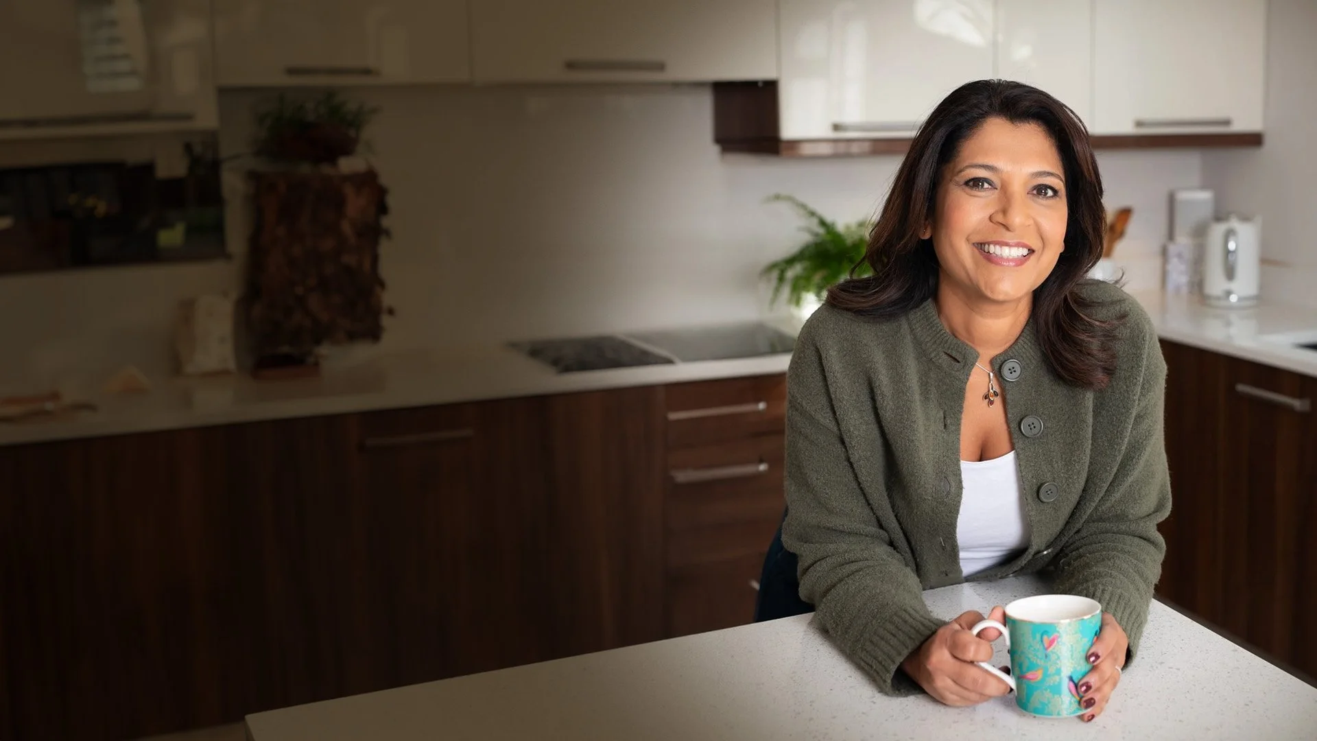 Navita Doshi smiling and holding a mug in a kitchen.