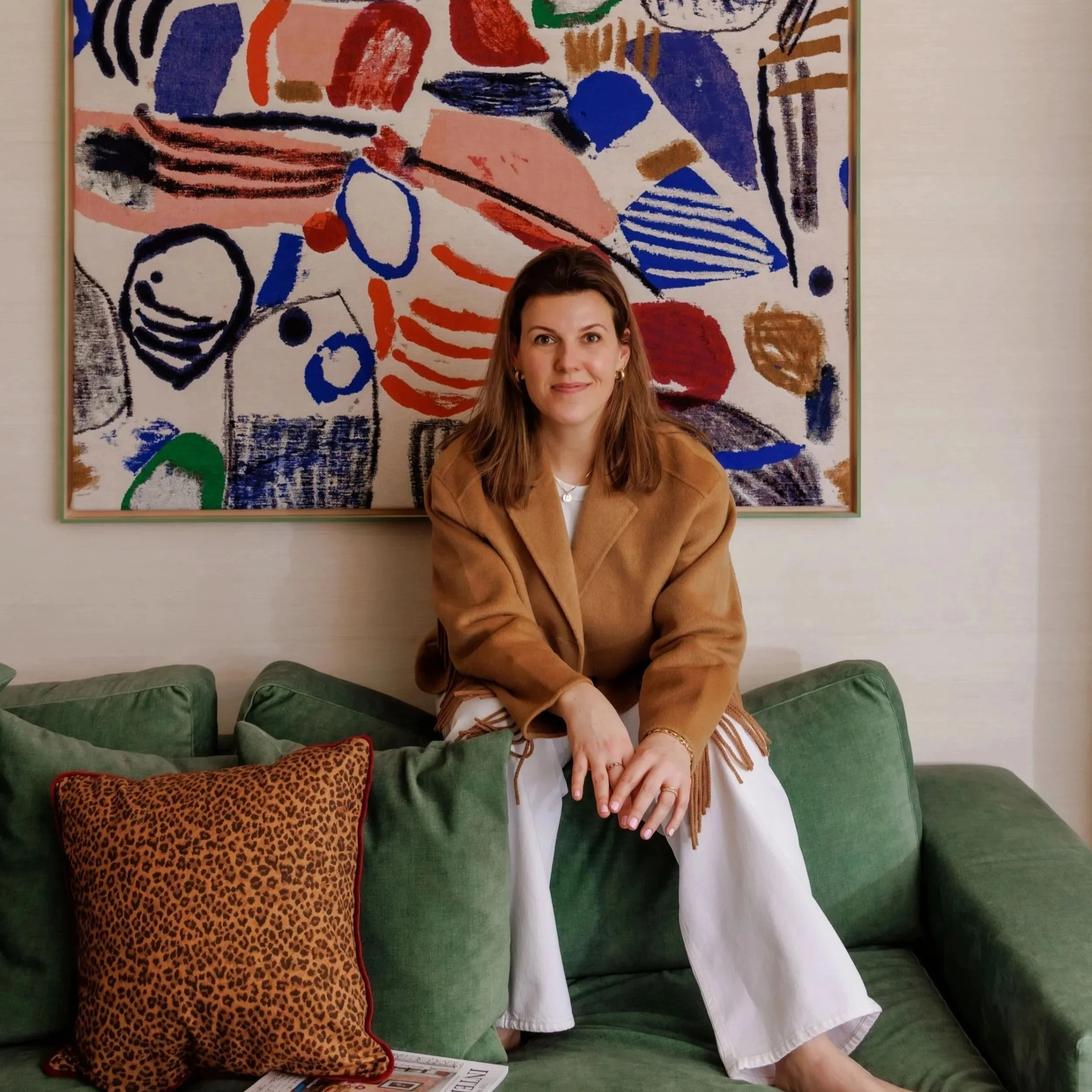 Annemijn van Atelier Sunday op een groene bank voor een kleurrijk abstract kunstwerk.