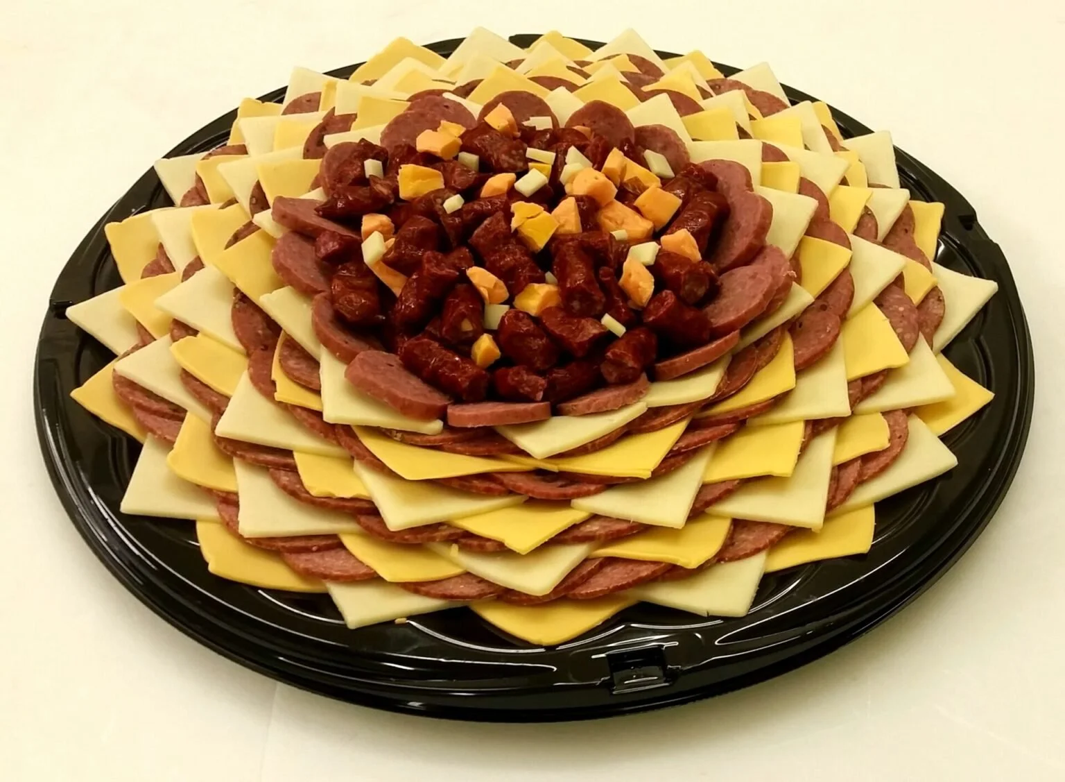 Layered tray of sliced cheeses, sliced meats, and a central mound of cooked chicken pieces topped with diced cheese.