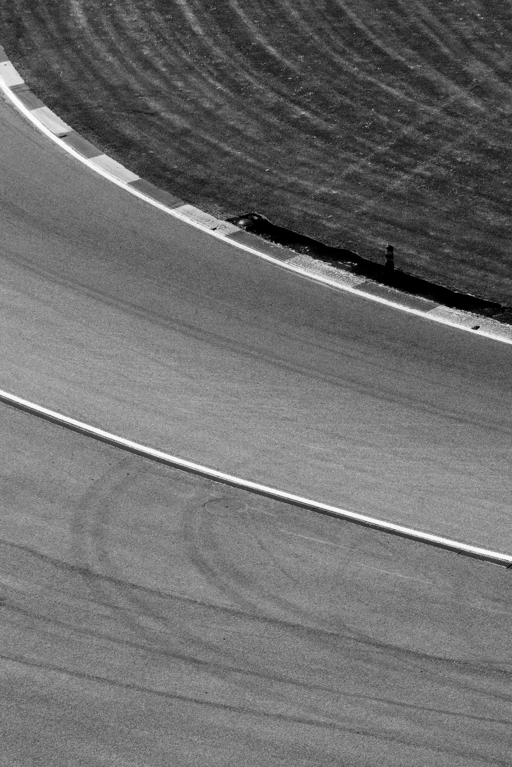 Close-up of a race track's asphalt surface and its curbing, taken from an aerial perspective, in black and white.