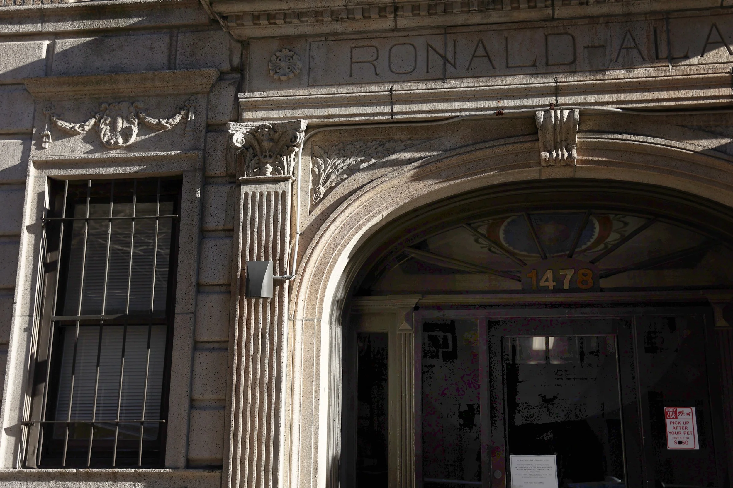 Close-up of an ornate building entrance with stone details, including an archway, decorative columns, and a sign reading 'Ronald' above the doorway. The address '1478' is visible on the arch.
