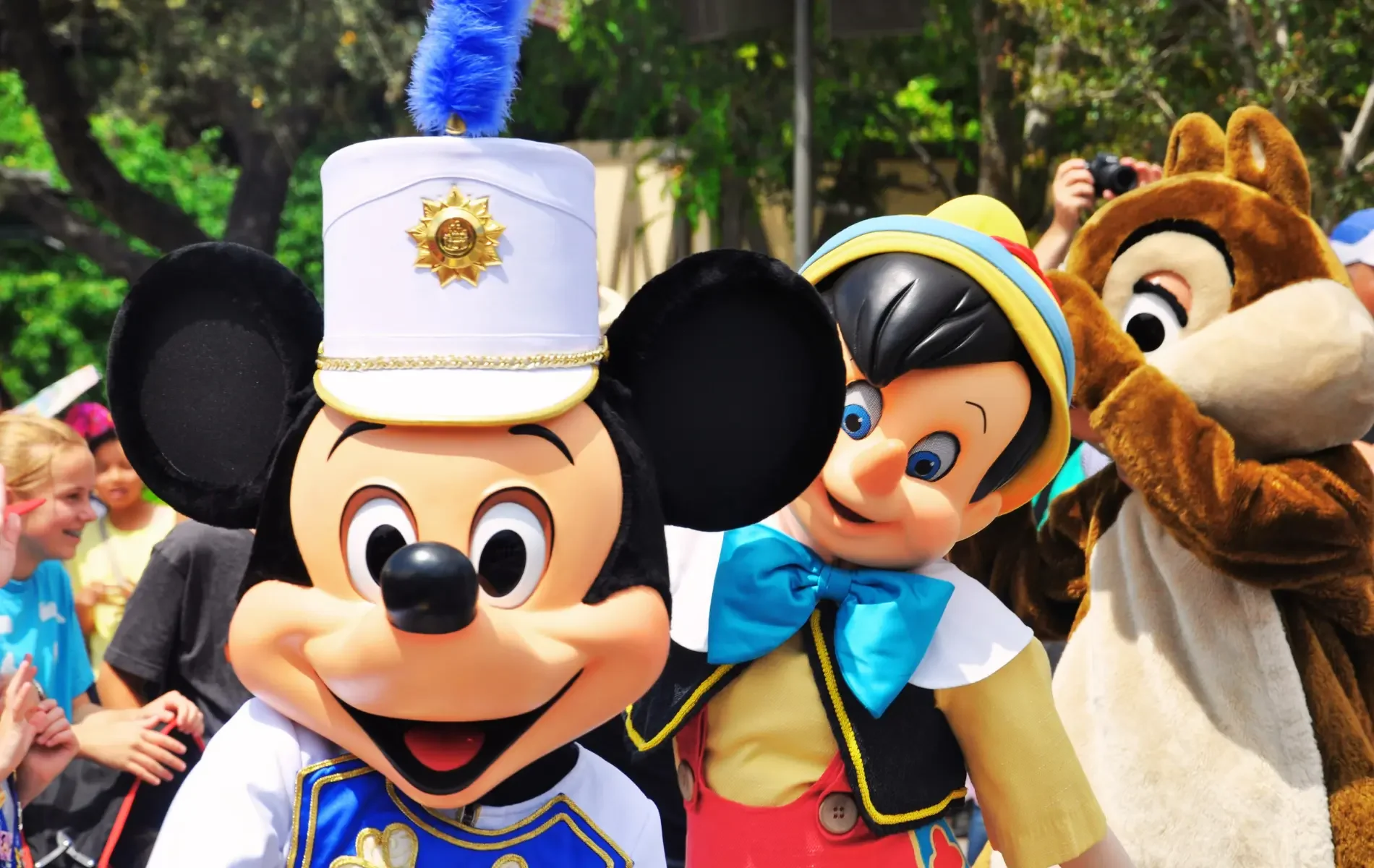 Mickey Mouse, Pinocchio, and a chipmunk mascot at a Disney park parade.