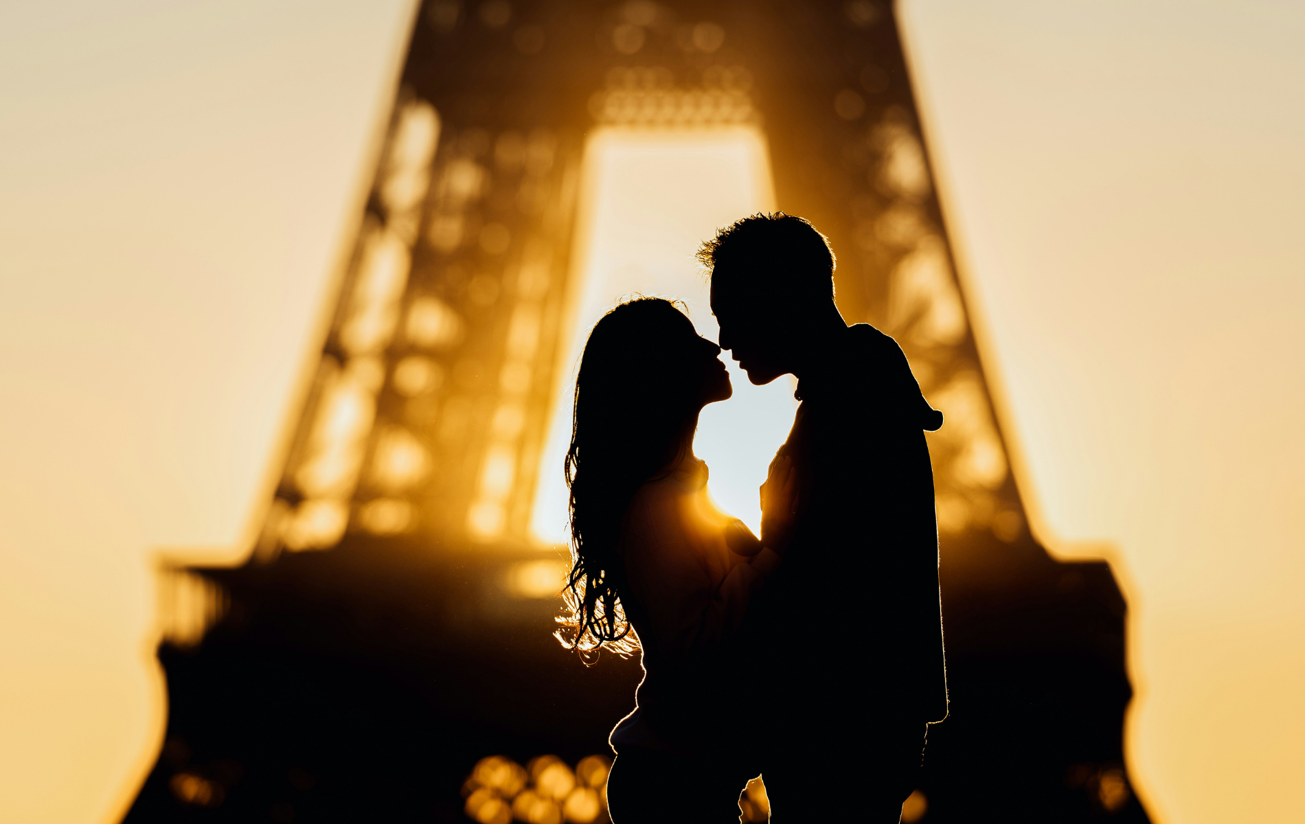 Silhouette of a couple kissing in front of the Eiffel Tower at sunset.