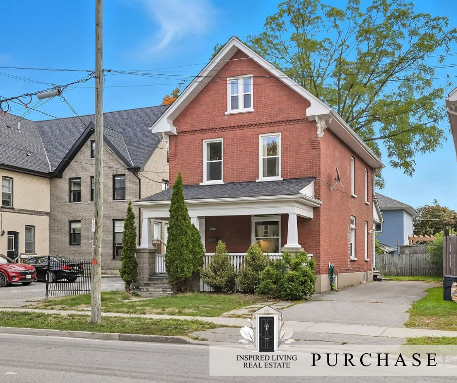A two-story red brick house with a front porch, white columns, and a gable roof, surrounded by trees and neighboring houses in a residential neighborhood.