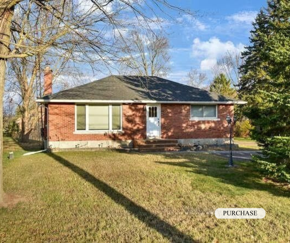 A single-story brick house with a gray roof, front steps, and a white door, surrounded by a green lawn and trees, on a sunny day.