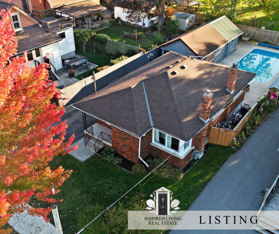 Aerial view of a brick house with two chimneys, a backyard with a shed, a swimming pool, and a porch surrounded by trees with fall foliage.