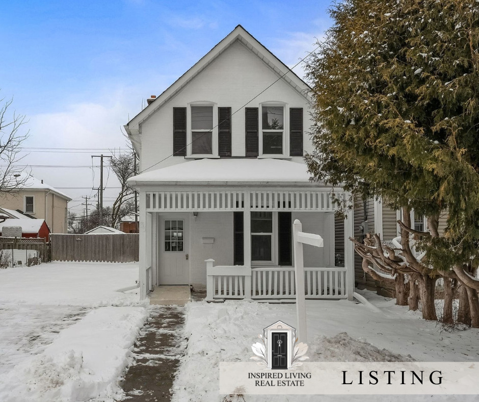 Two-story white house with black shutters, covered porch, snow on the ground, and a tree on the right side.