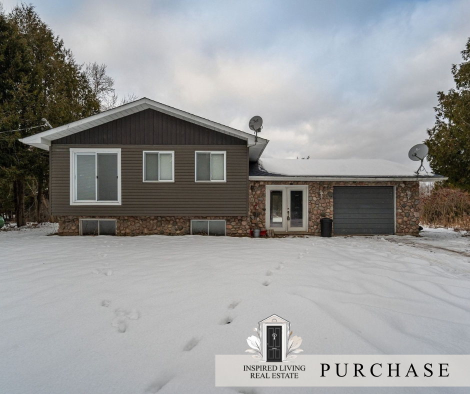 A house with a brown exterior, a stone base, a grey garage door, and snow-covered ground.