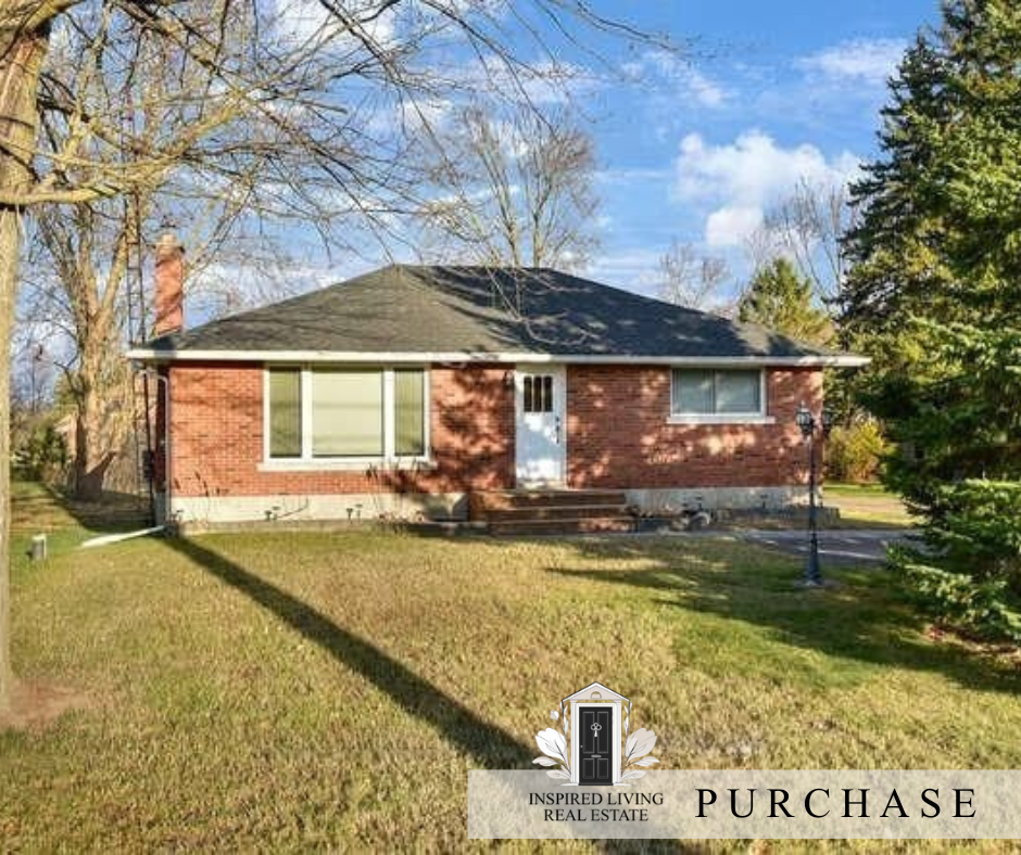 Front view of a single-story brick house with a dark roof, white front door, and large window, surrounded by trees, with a lawn and pathway leading to the entrance.