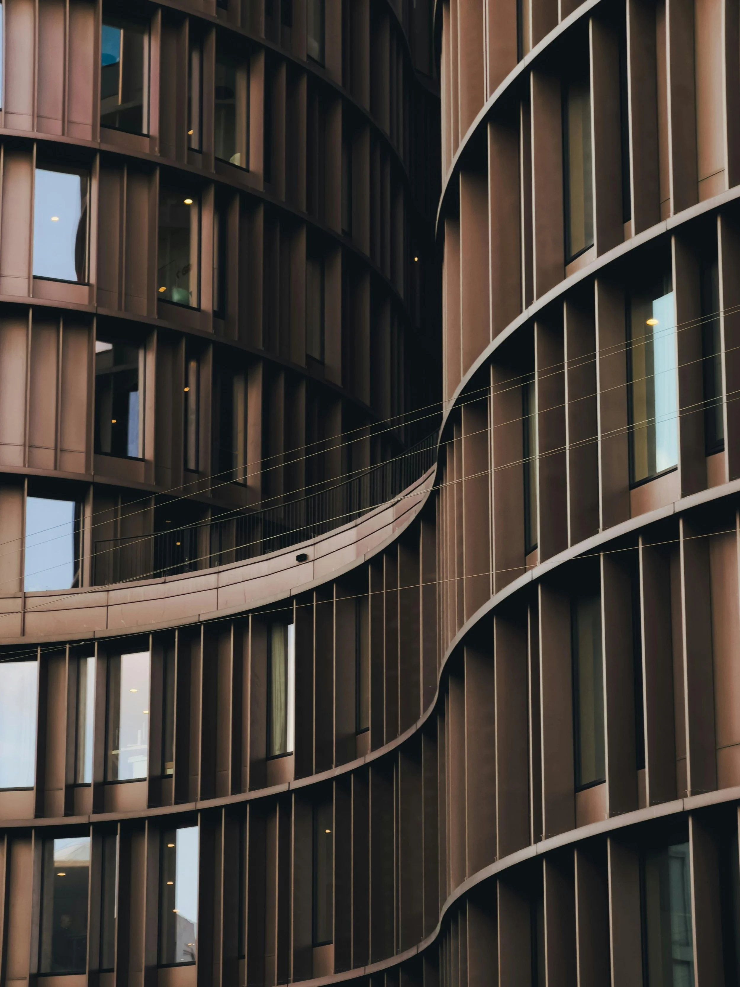 Modern multi-story building with curved glass and metal exterior, featuring rows of windows and vertical design elements.