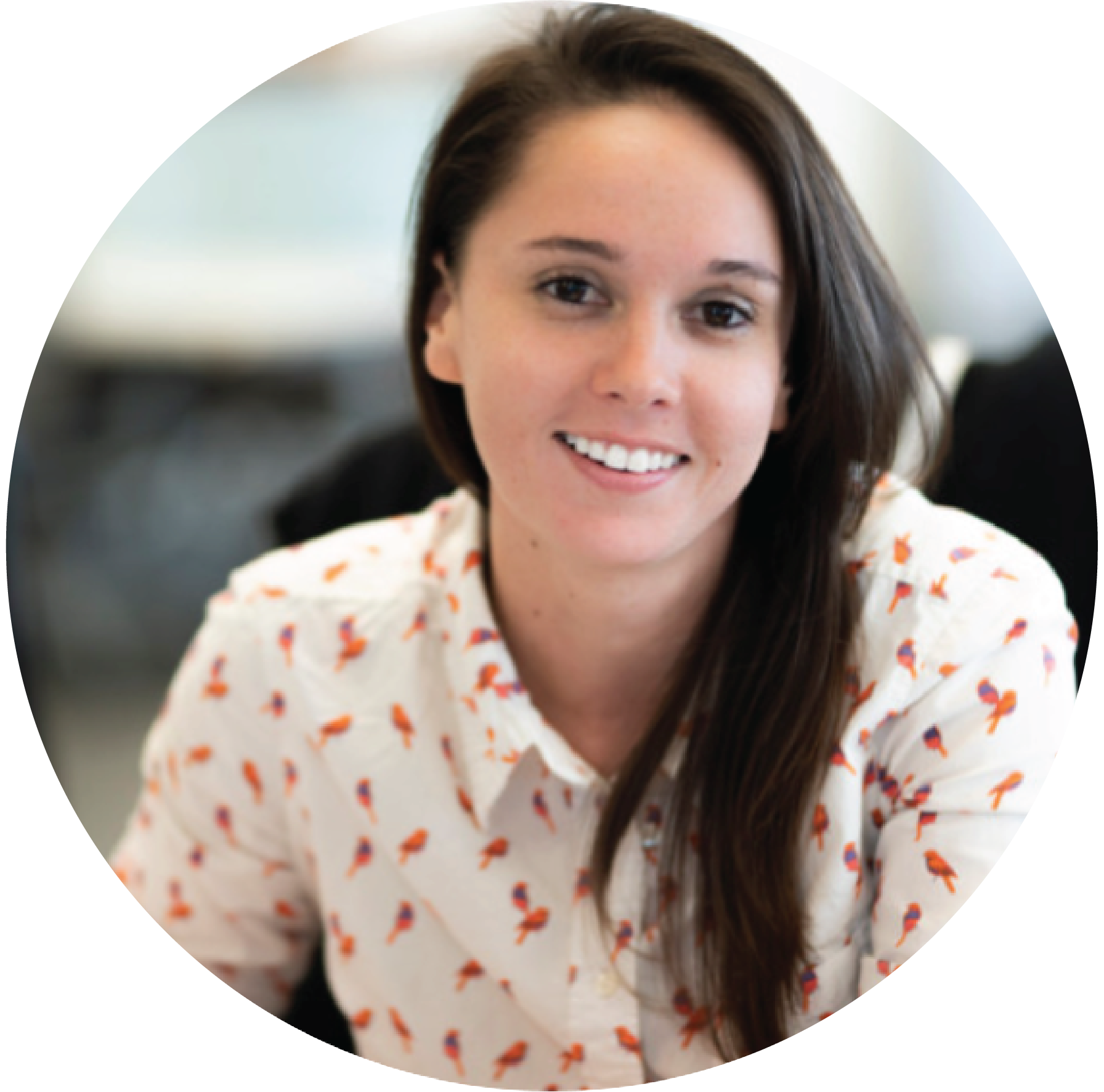 A smiling woman with long brown hair wearing a white blouse with small orange and blue patterns.