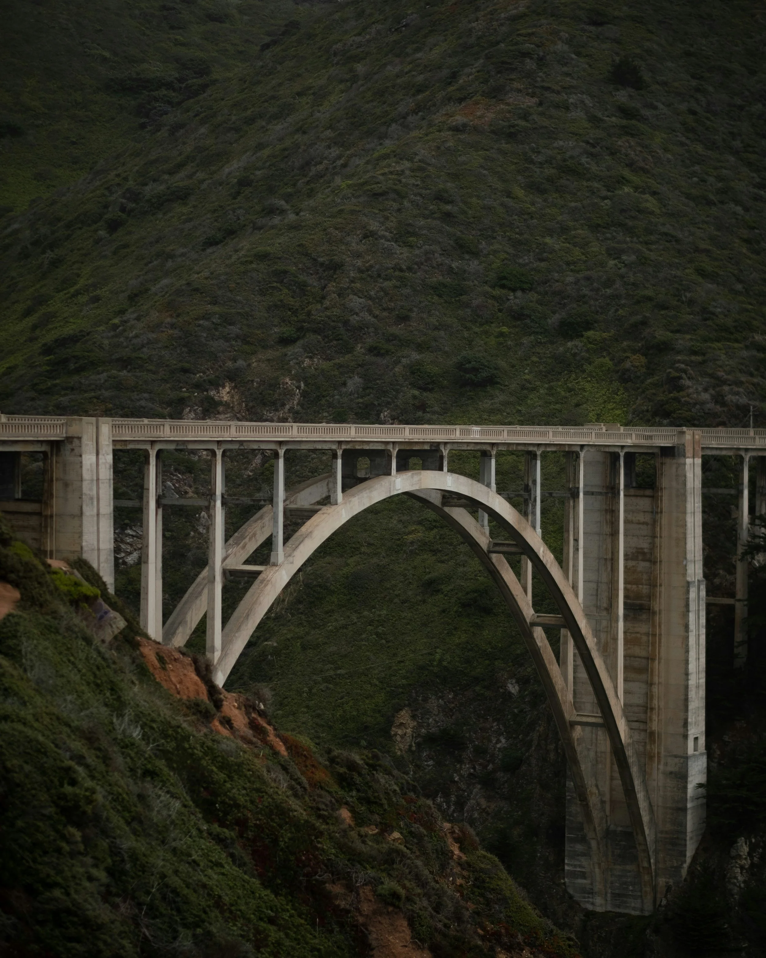 A large concrete arch bridge crossing a steep green hillside.