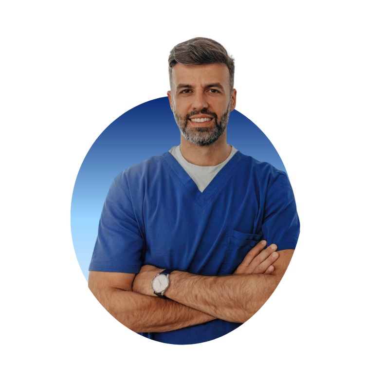 A smiling middle-aged man with gray hair and beard wearing blue medical scrubs, standing with arms crossed against a plain background.